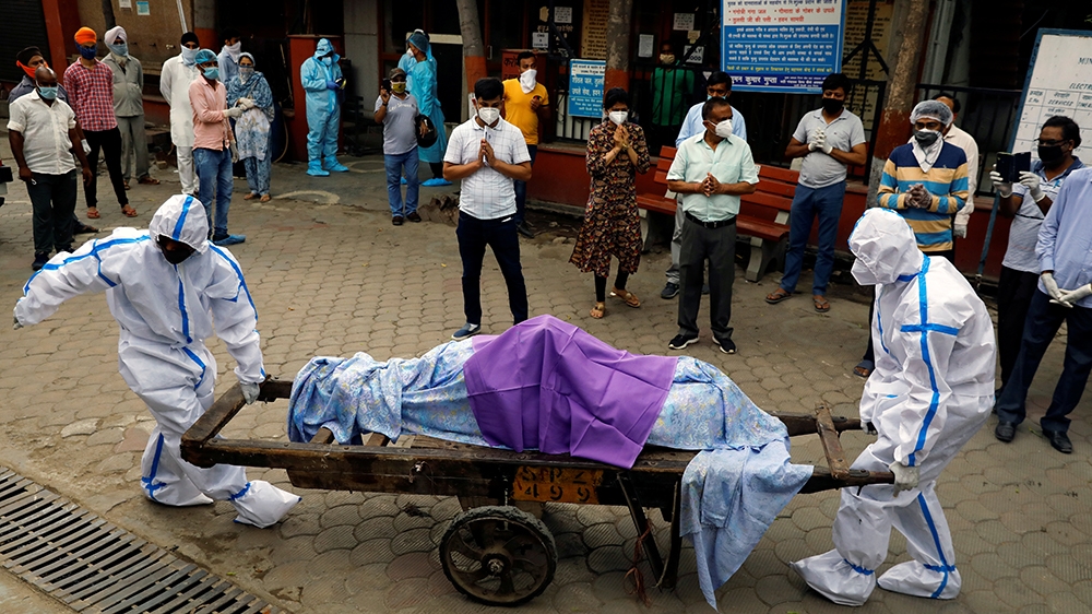 Health workers wearing personal protective equipment carry the body of a person who died from COVID-19 to a crematorium in New Delhi