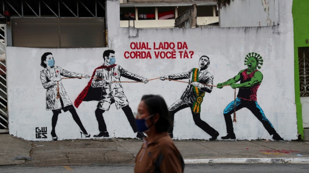 A woman walking past a graffiti of Brazilian President Jair Bolsonaro and a person depicting the coronavirus pulling a rope against health workers in Sao Paulo, Brazil; the graffiti reads: ‘Which side are you on?’