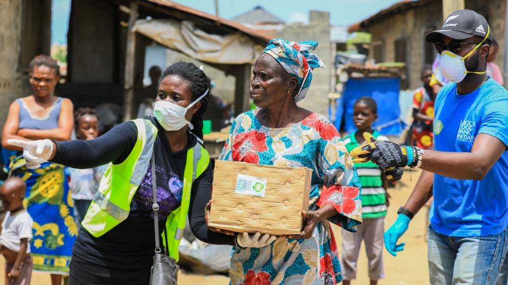 Volunteers gesture as they direct an elderly woman at an ongoing distribution of food parcels