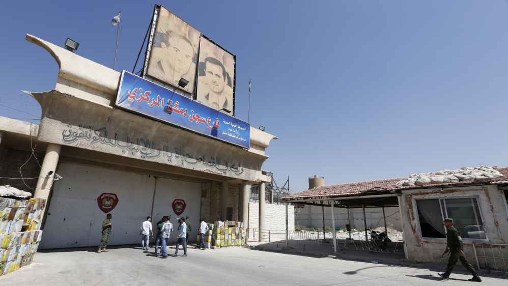 Members of Syrian security services and journalists stand at the entrance of the central prison, after it was targeted by mortar shells fired by rebels, in Damascus