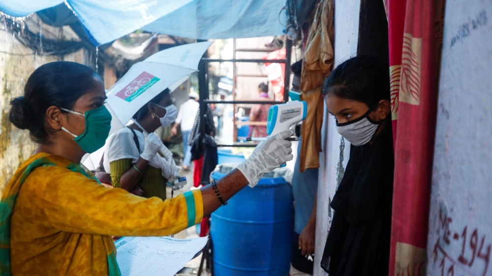 A community health volunteer checks the temperature of a girl during a check-up campaign for the coronavirus at a slum in Mumbai