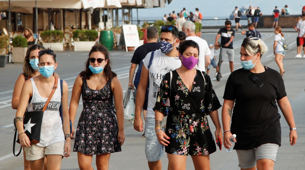 People wear masks as they walk on the street following a government decree that face coverings must be worn between 6 p.m. and 6 a.m. in areas close to bars and pubs and where gatherings are more like