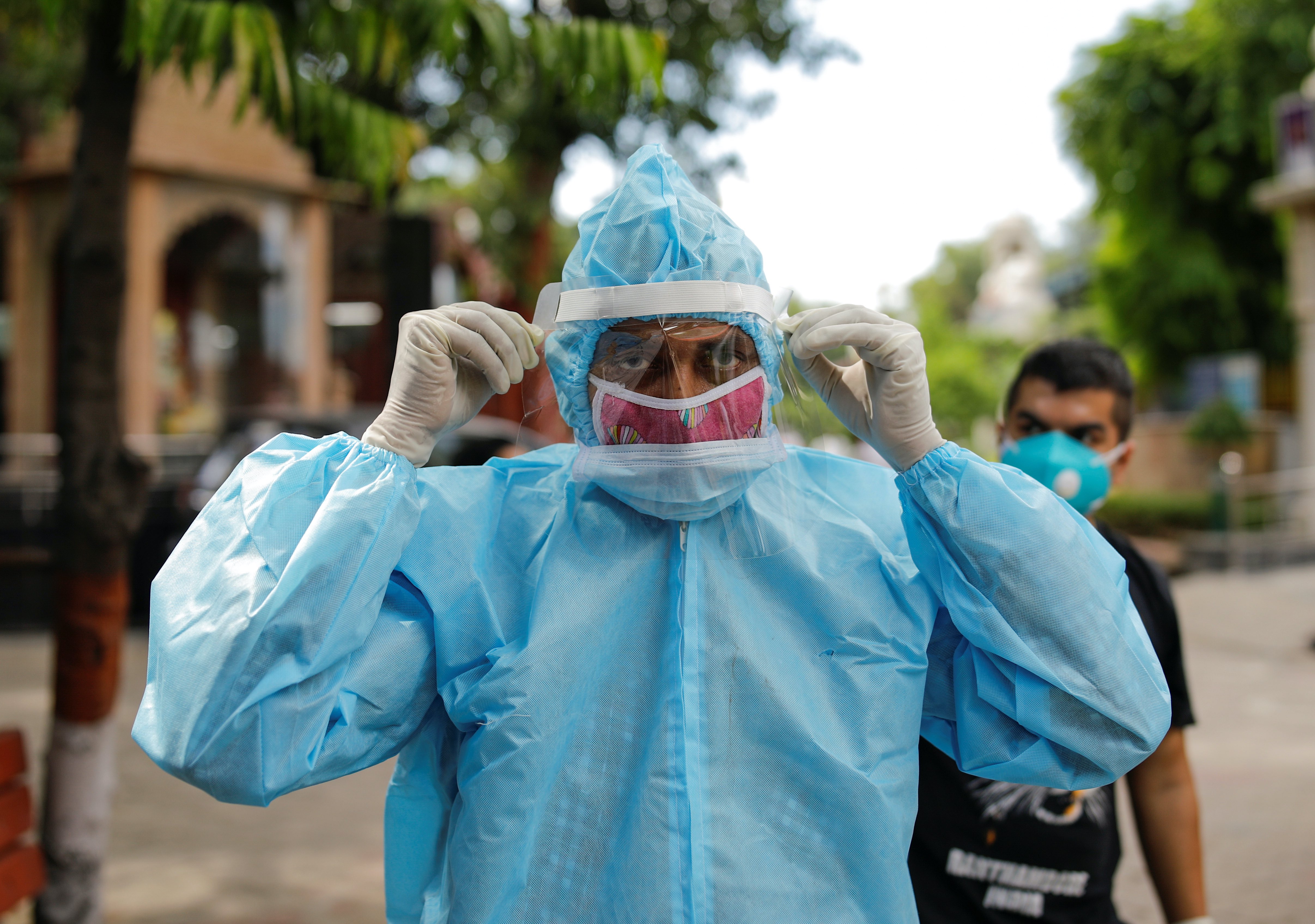 A relative wearing personal protective equipment adjusts his protective face shield before the cremation of a man who died due to coronavirus at a crematorium in New Delhi, India