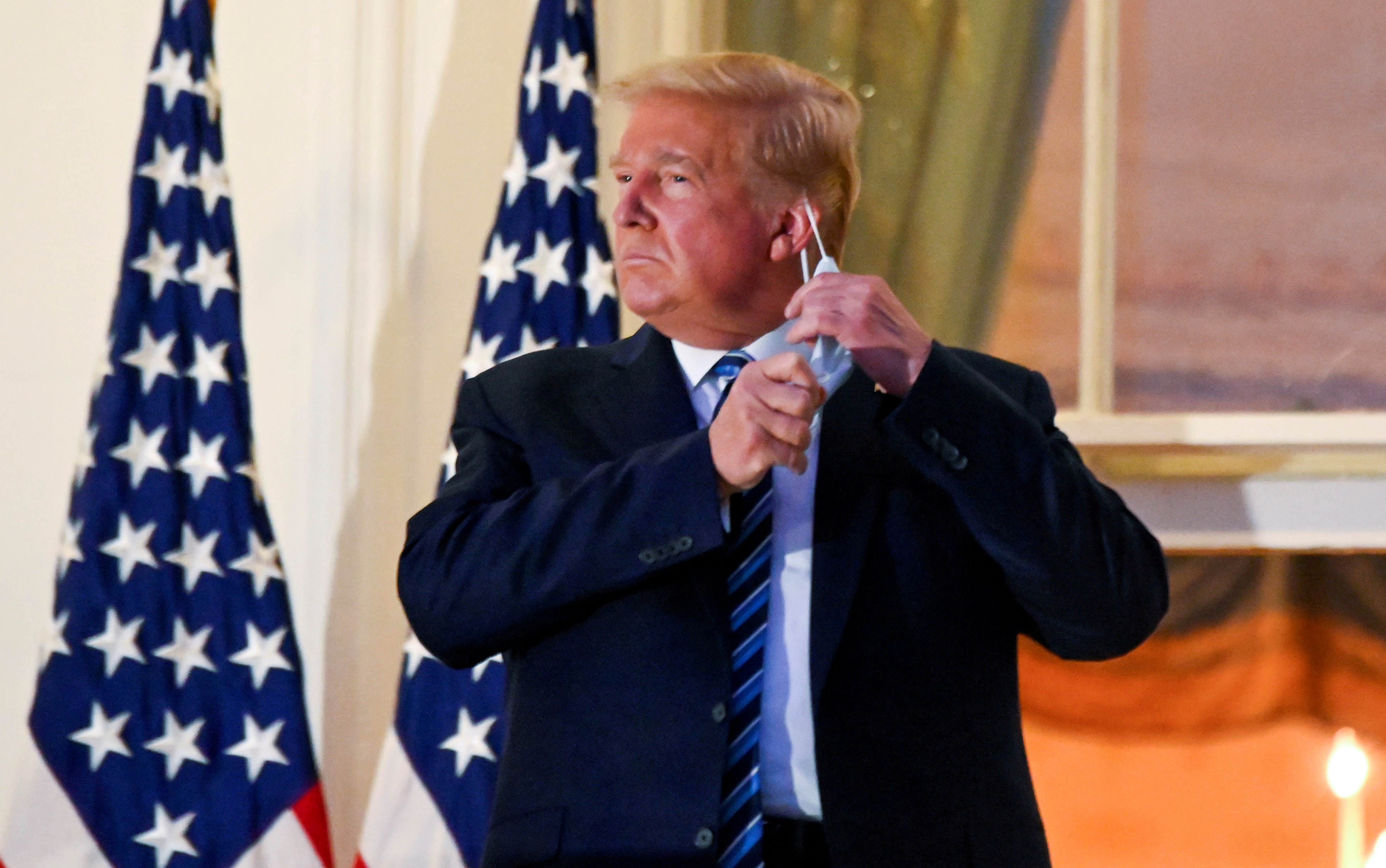 President Donald Trump pulls off his protective face mask as he poses atop the Truman Balcony of the White House after returning from being hospitalised at Walter Reed Medical Center