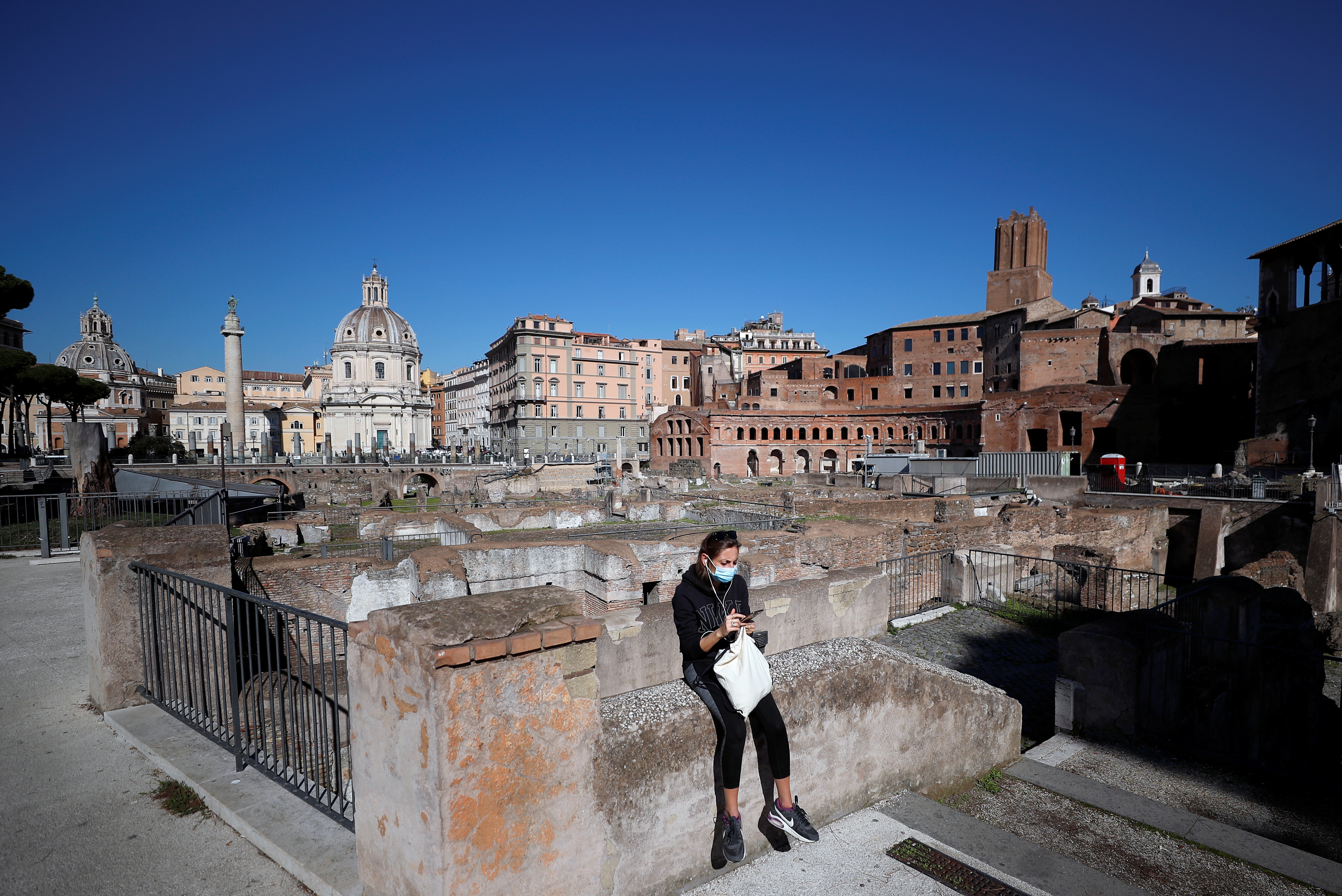 A woman wearing a face mask sits near the Roman Forum as Italy is facing a surge in coronavirus infections, in Rome