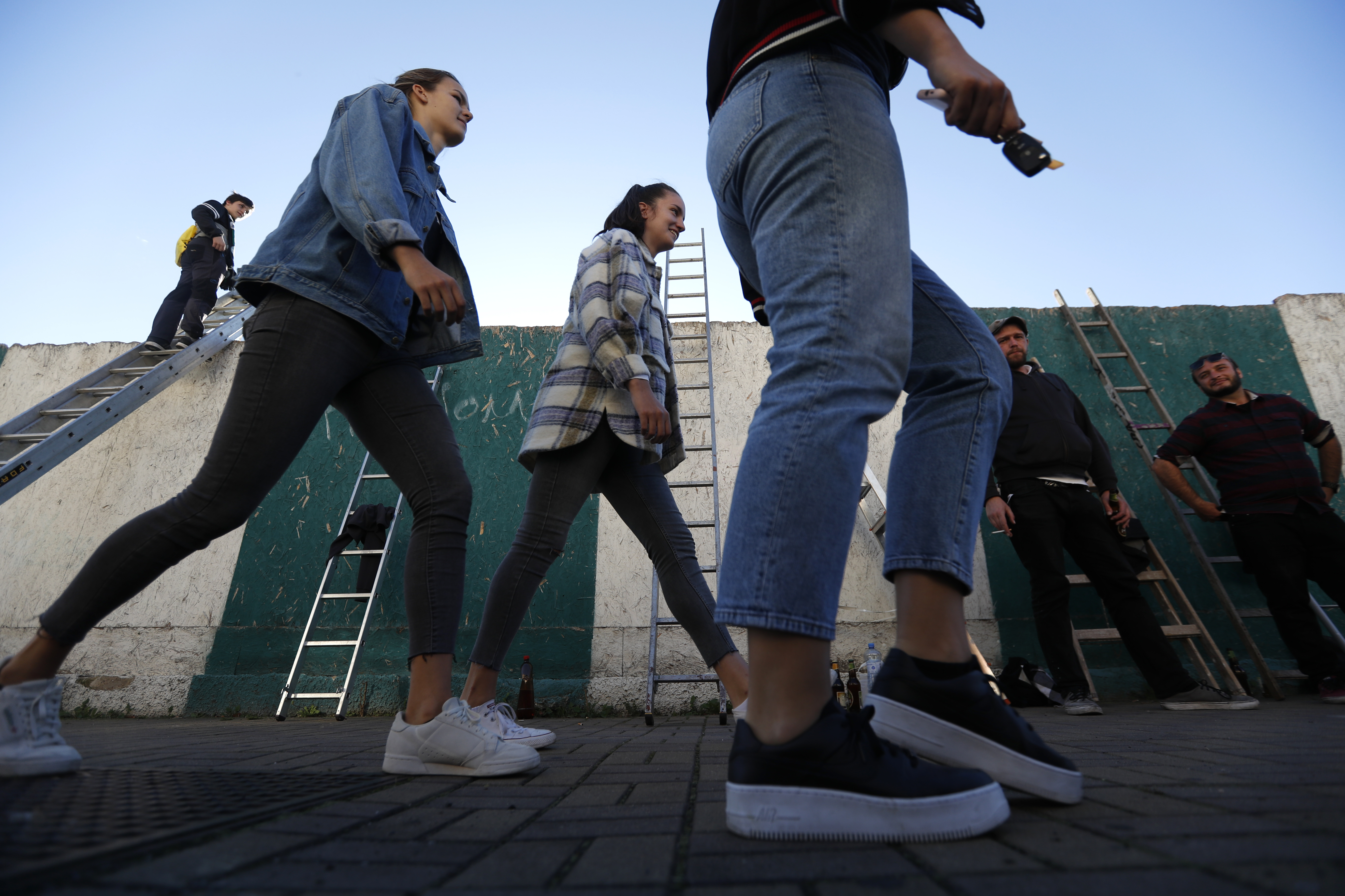Women walk past fans standing by their ladders before watching a Czech first division match between Bohemians Prague and Zlin in Prague, Czech Republic. Amid restrictive measures that limit the number of football fans from attending the game, fans are looking for innovative ways to watch