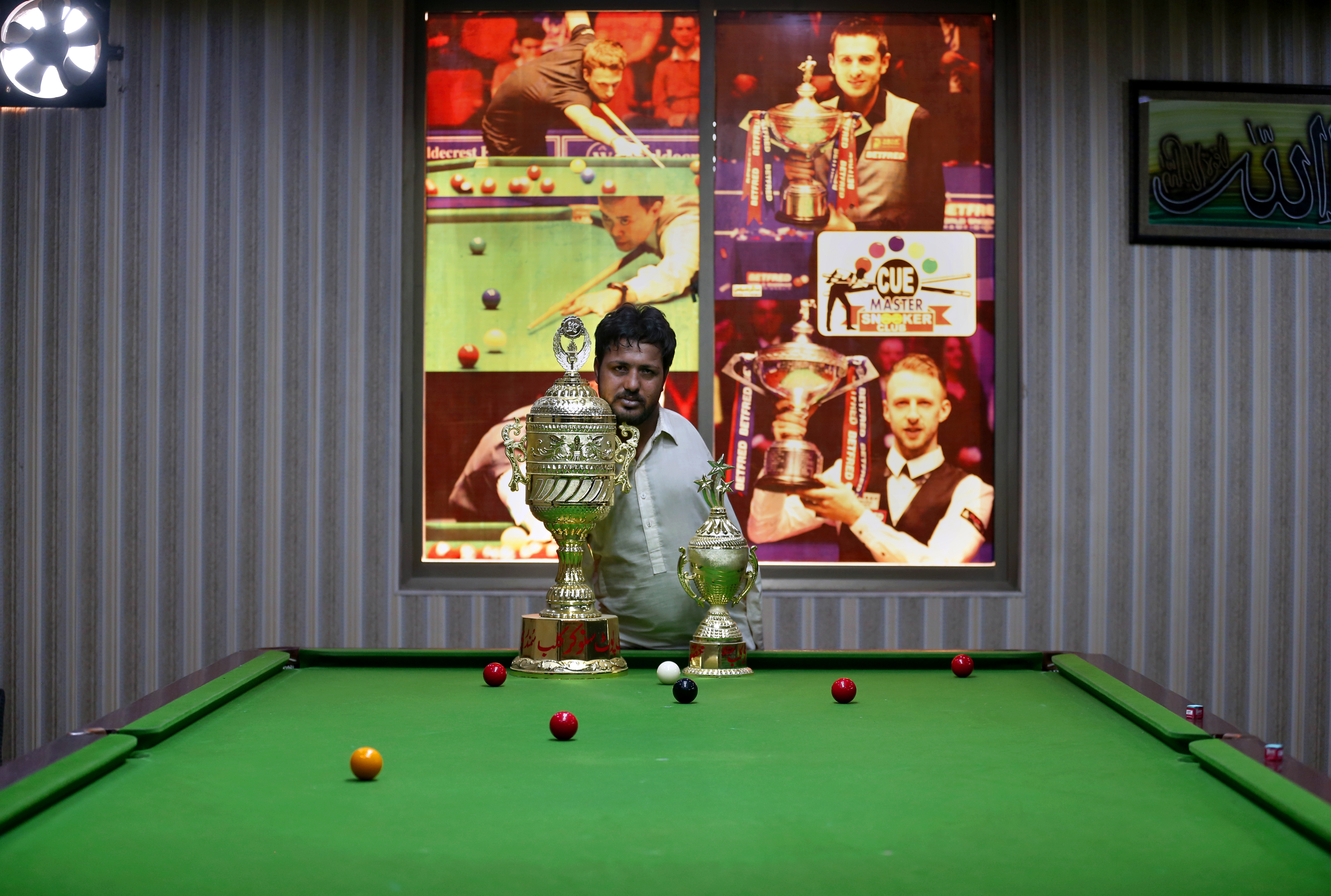 Mohammad Ikram, who play snooker with his chin, poses for a photograph with his trophies at a local snooker club in Samundri, Pakistan