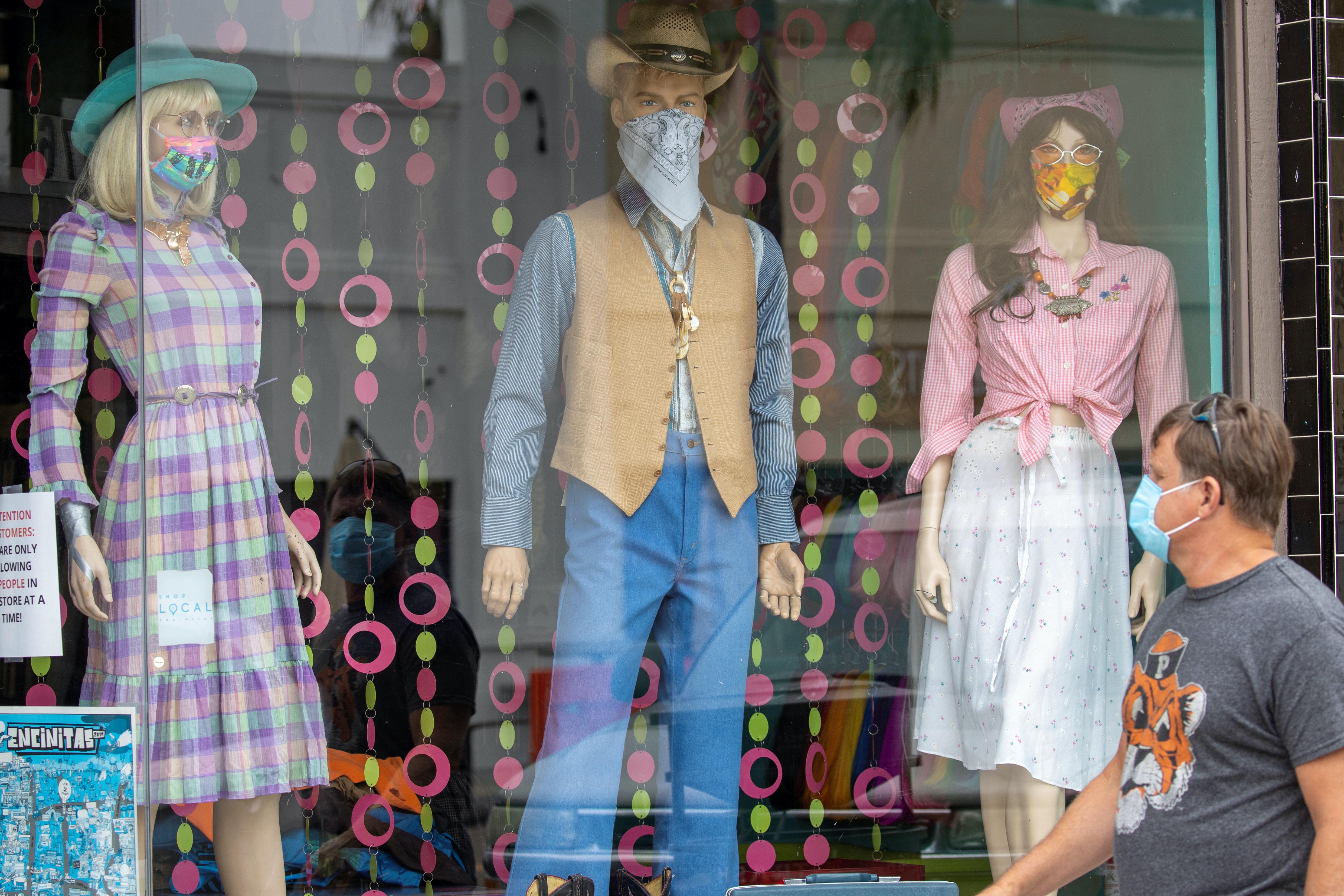 A man wears a mask as he walks past mannequins wearing masks in a retail shopping area during the outbreak of the coronavirus in Encinitas, California, United States