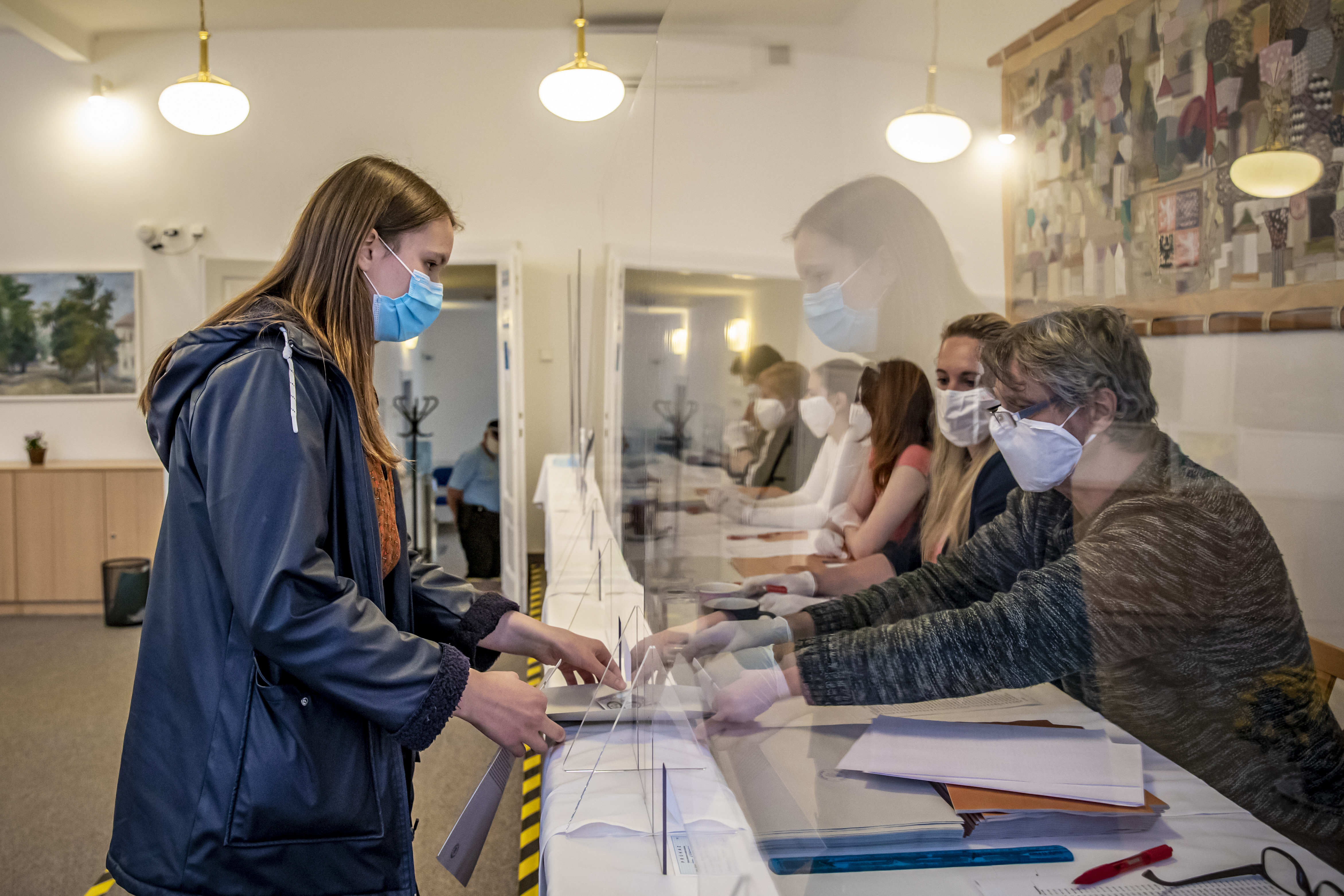 A voter wearing protective face mask talks to election committee members through protective shield during the regional and senate elections in Pruhonice, on October 2