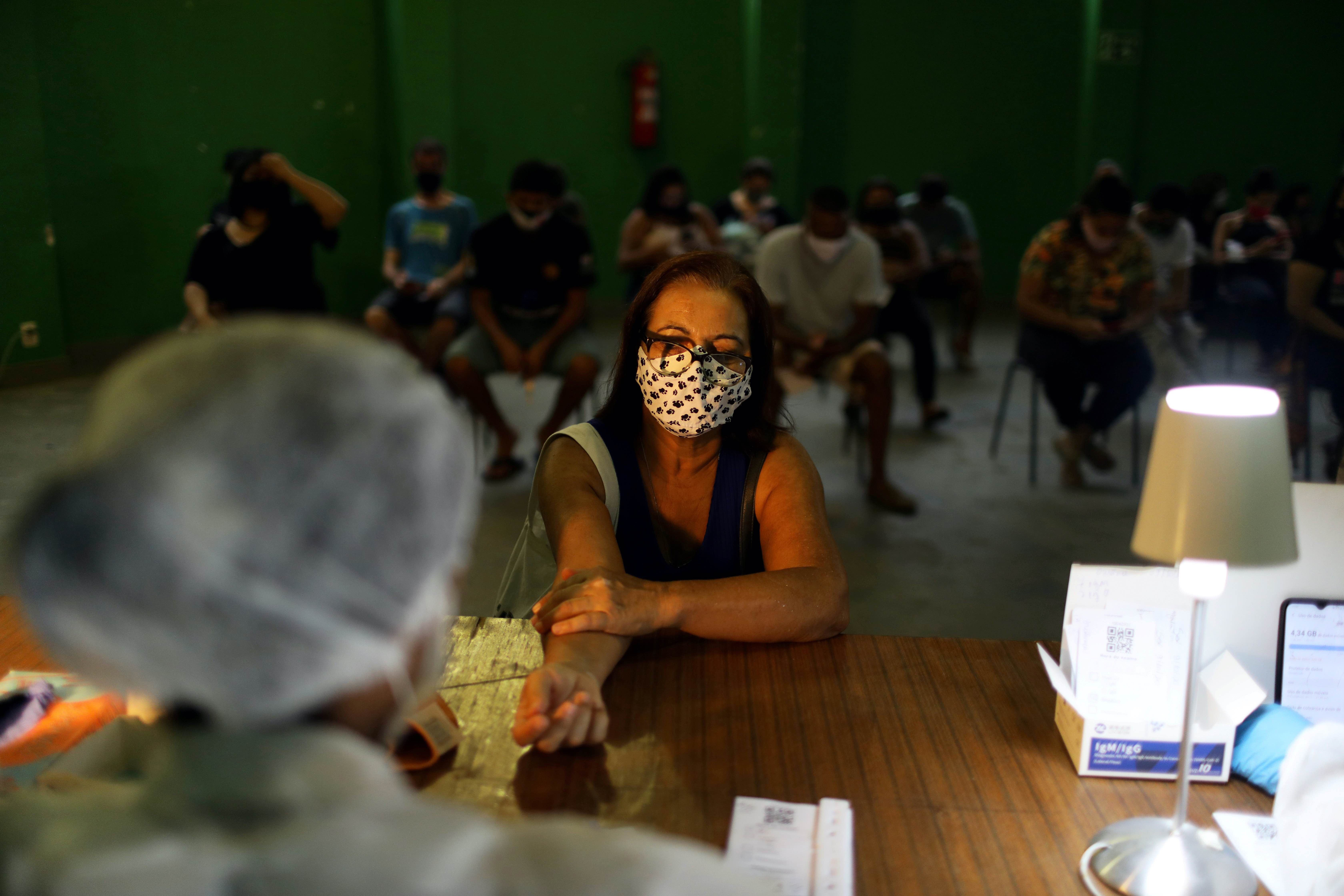 A nurse takes a blood sample from a woman for a coronavirus test at the Santa Marta slum in Rio de Janeiro, Brazil