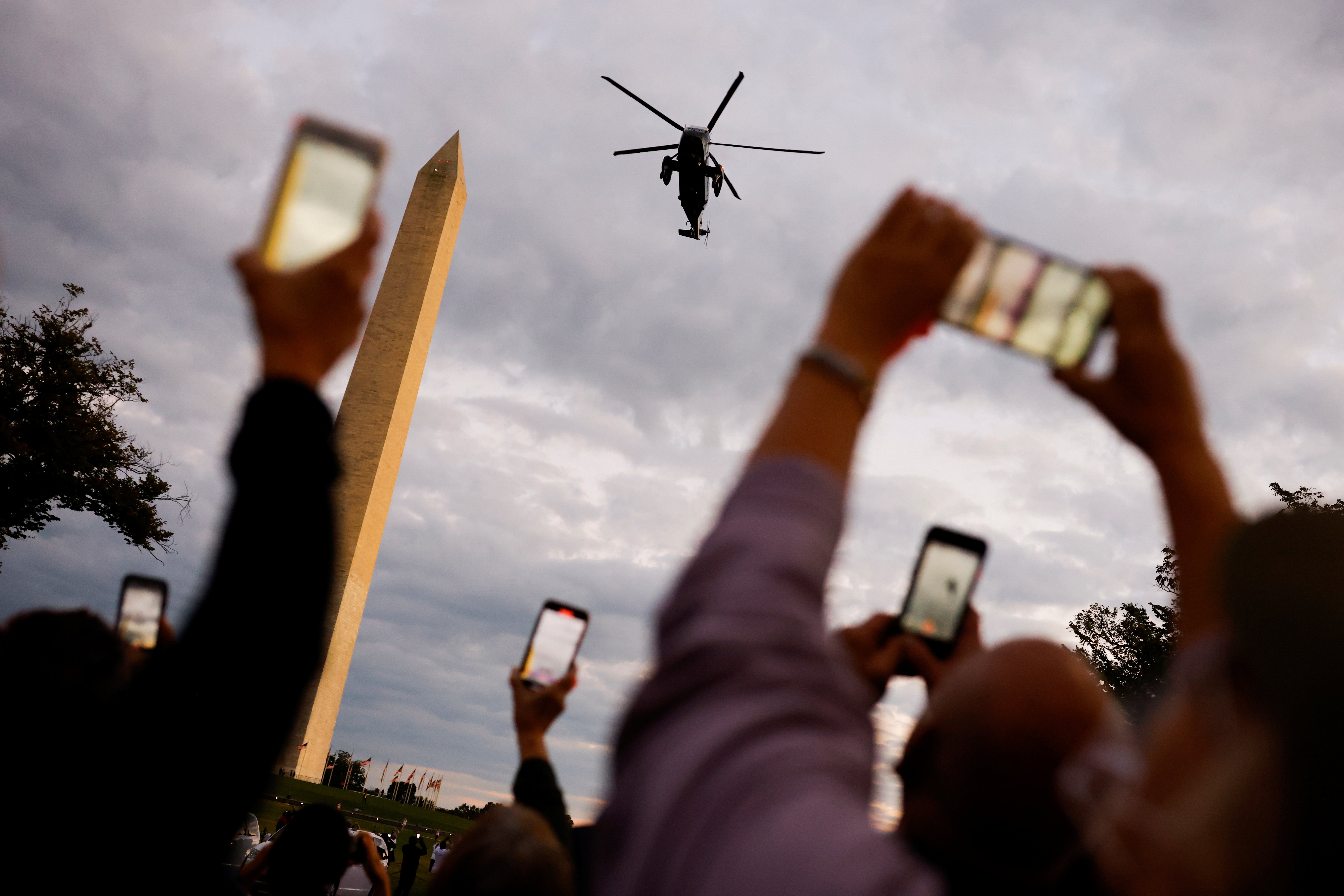 People take pictures of a Marine One helicopter with US President Donald Trump aboard as it flies to the White House after the president underwent treatment for the coronavirus in Washington, DC, the US