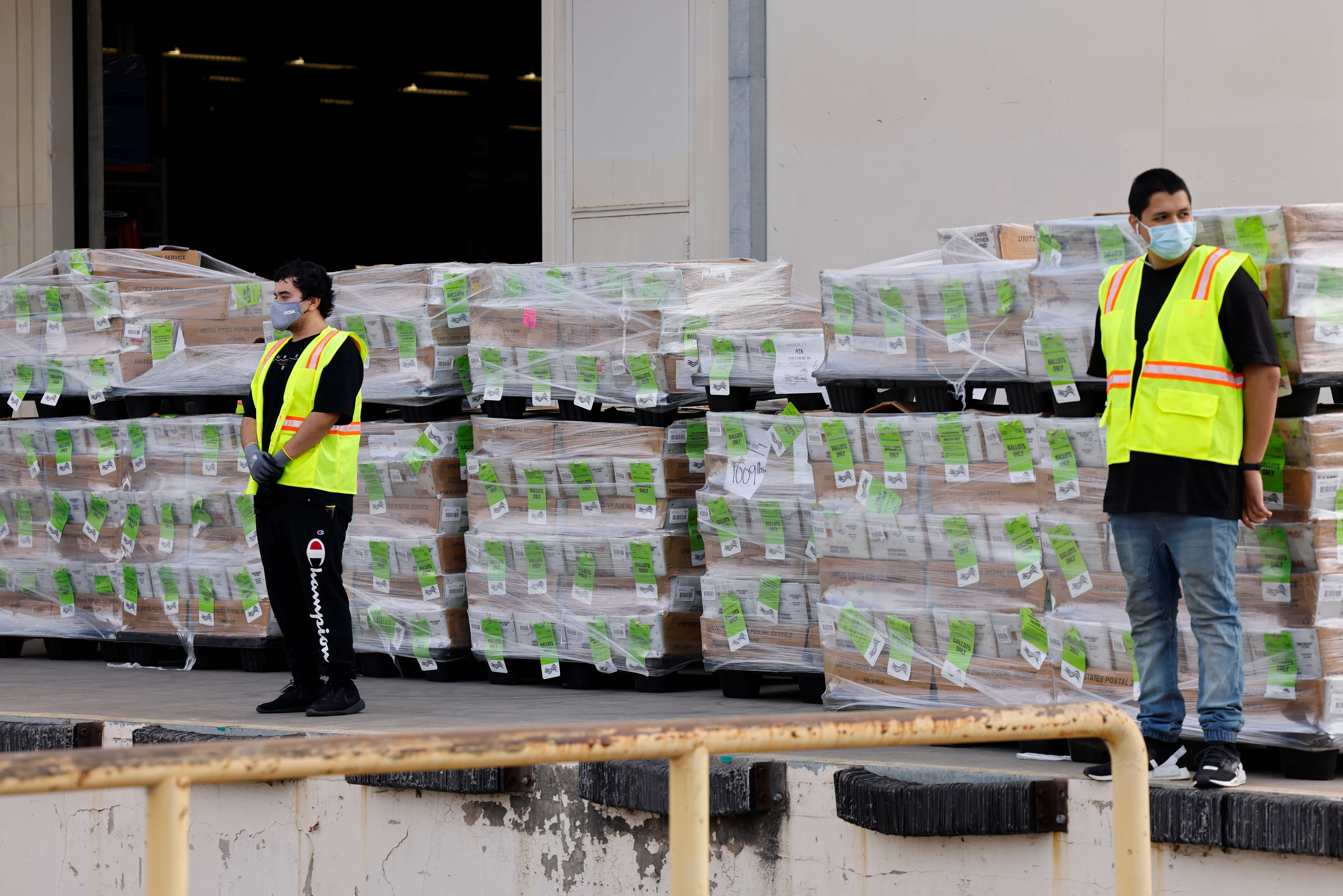 Workers stand next to pallets of mail-in election ballots at the Orange County Registrar of Voters before the ballots are shipped to the US Postal Service for delivery to voters in Santa Ana, California, the US
