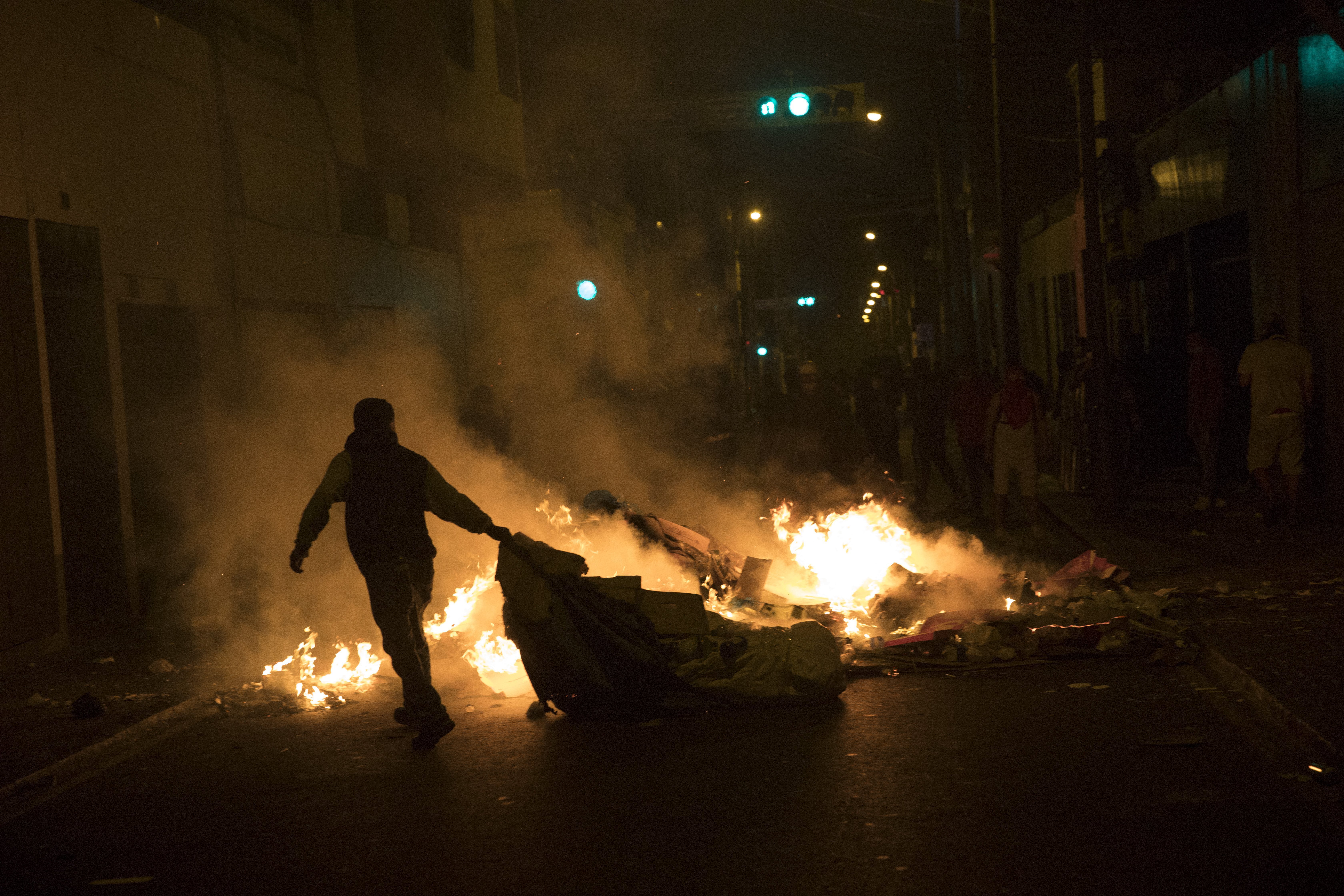 A protester drags cardboard into a fire during in Lima, Peru on Saturday night