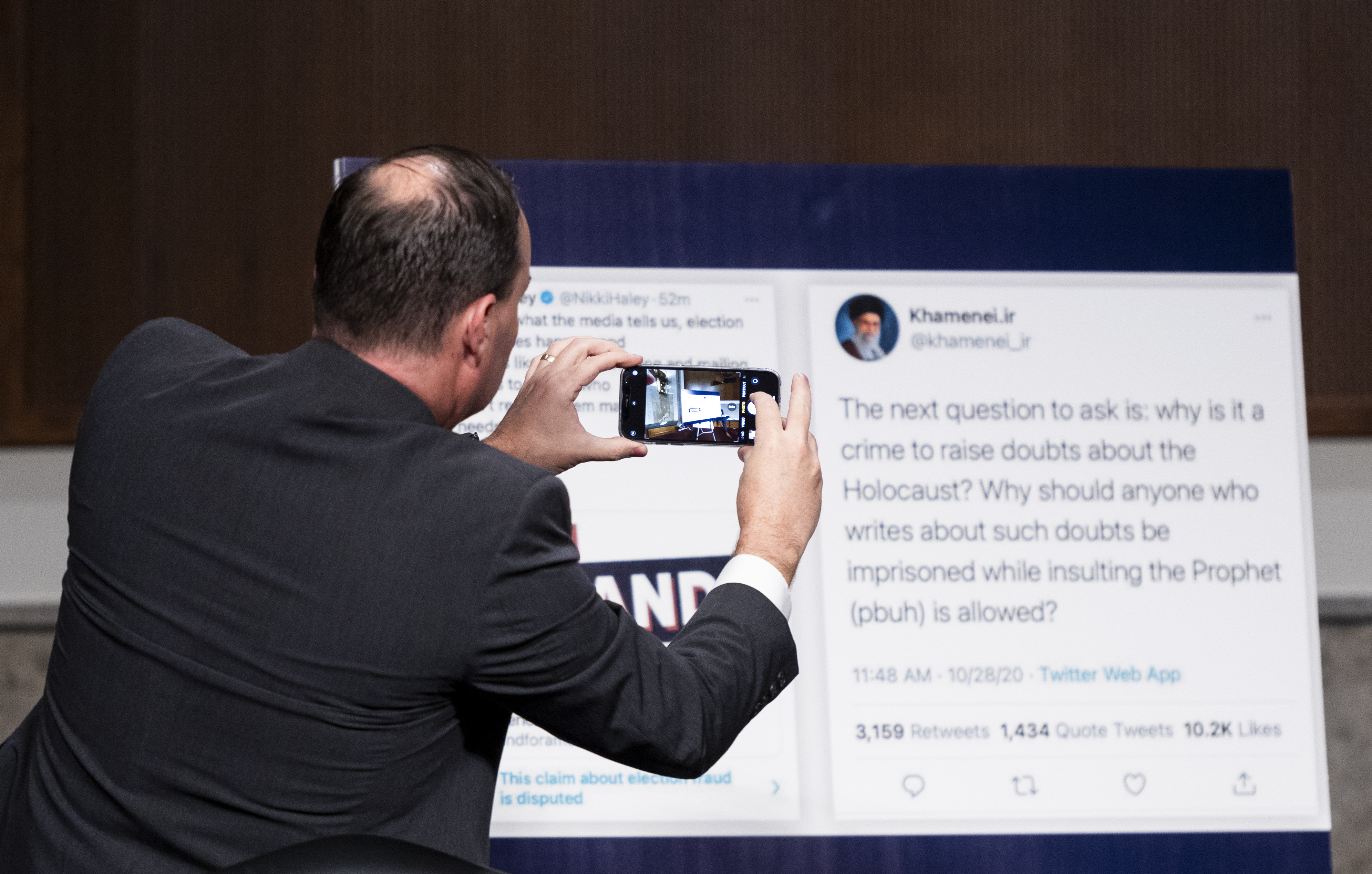 Senator Mike Lee takes a photo of a display before a Senate Judiciary Committee hearing on the actions of Facebook and Twitter surrounding the election