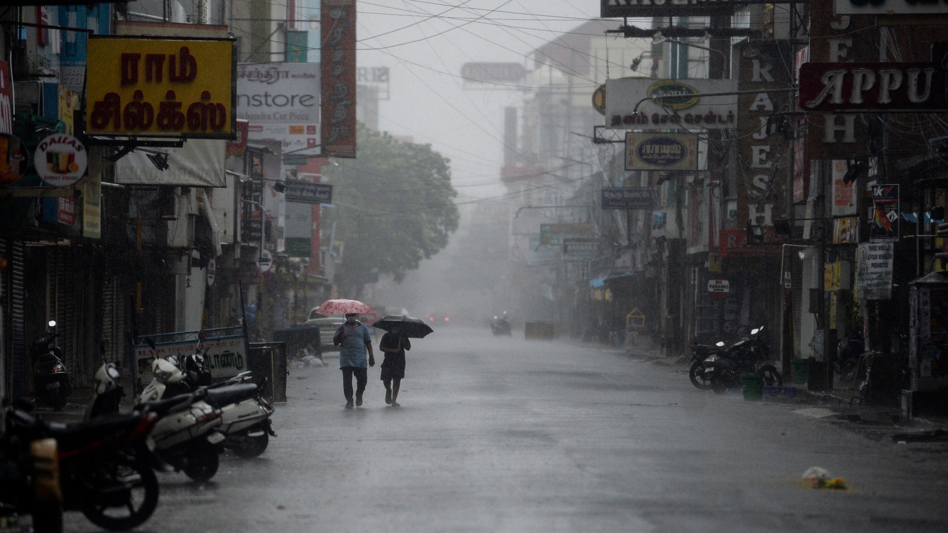 Residents shelter from heavy rain under umbrellas while walking along a deserted road as cyclone Nivar approaches the southeastern Indian coast in Puducherry