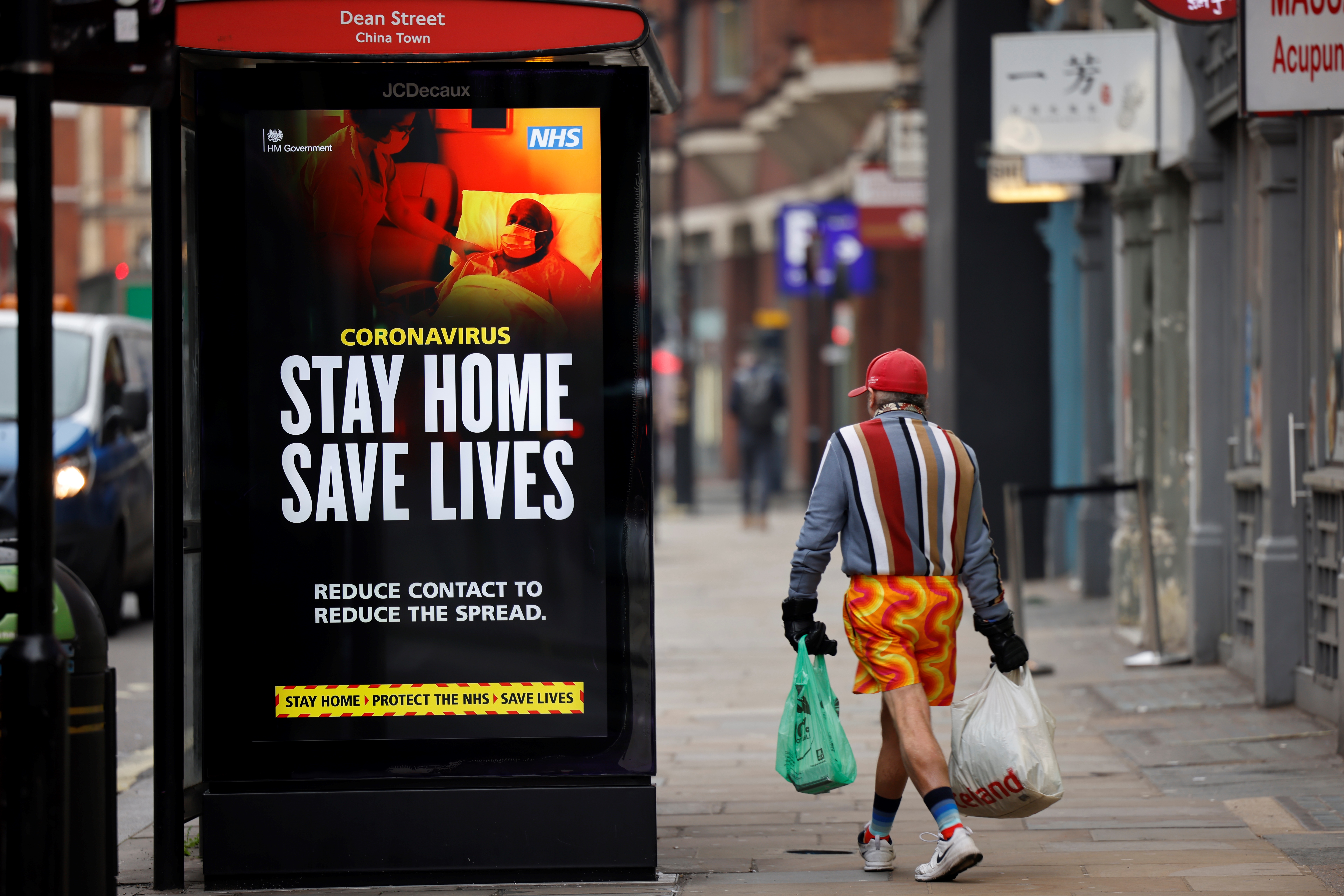 A shopper walks past NHS signage promoting ‘Stay Home, Save Lives’ on a bus shelter in Chinatown, central London