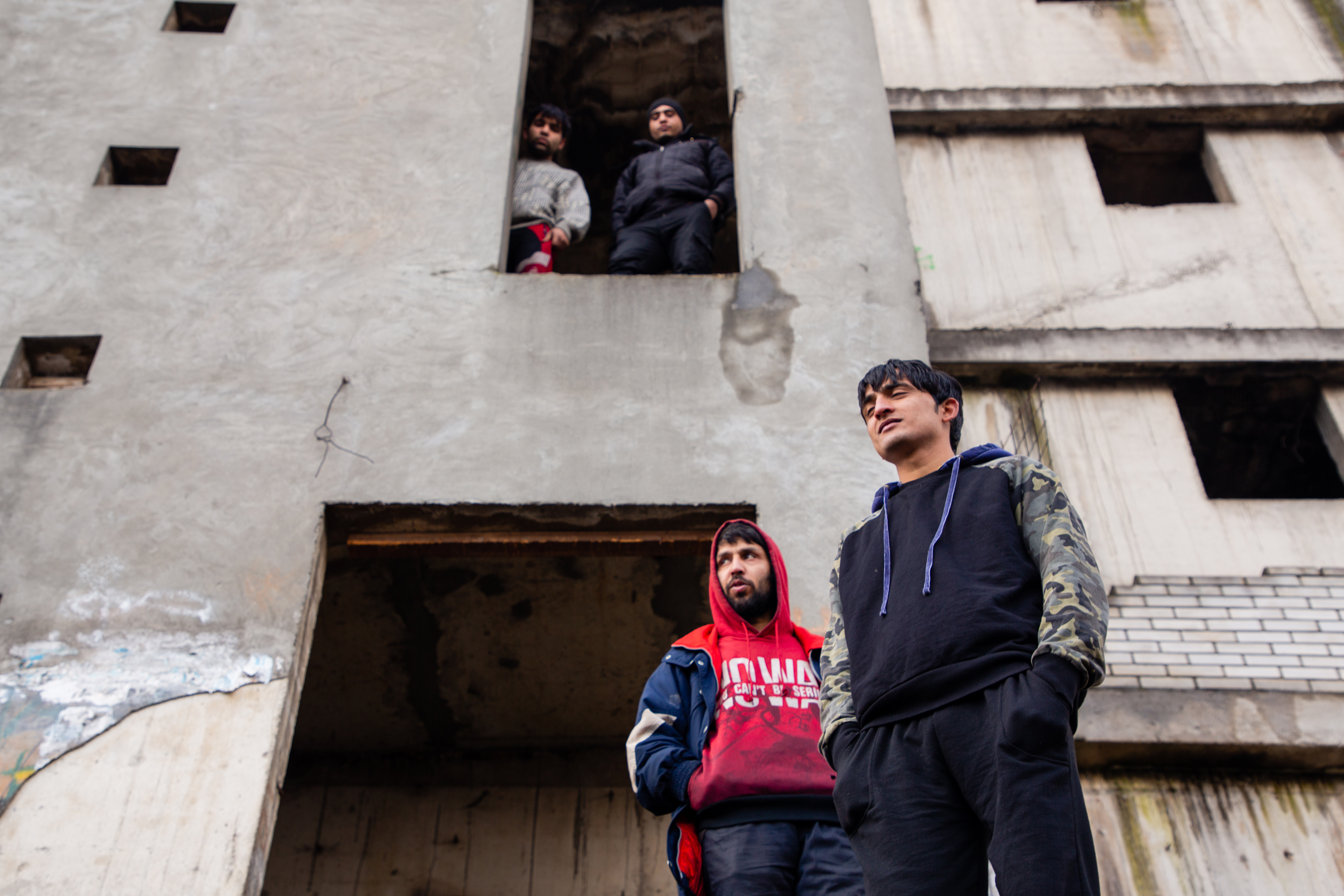 Refugees stand in front of the Dom Penzionera building in downtown Bihać, on the banks of the Una River. [Elisa Oddone/Al Jazeera]