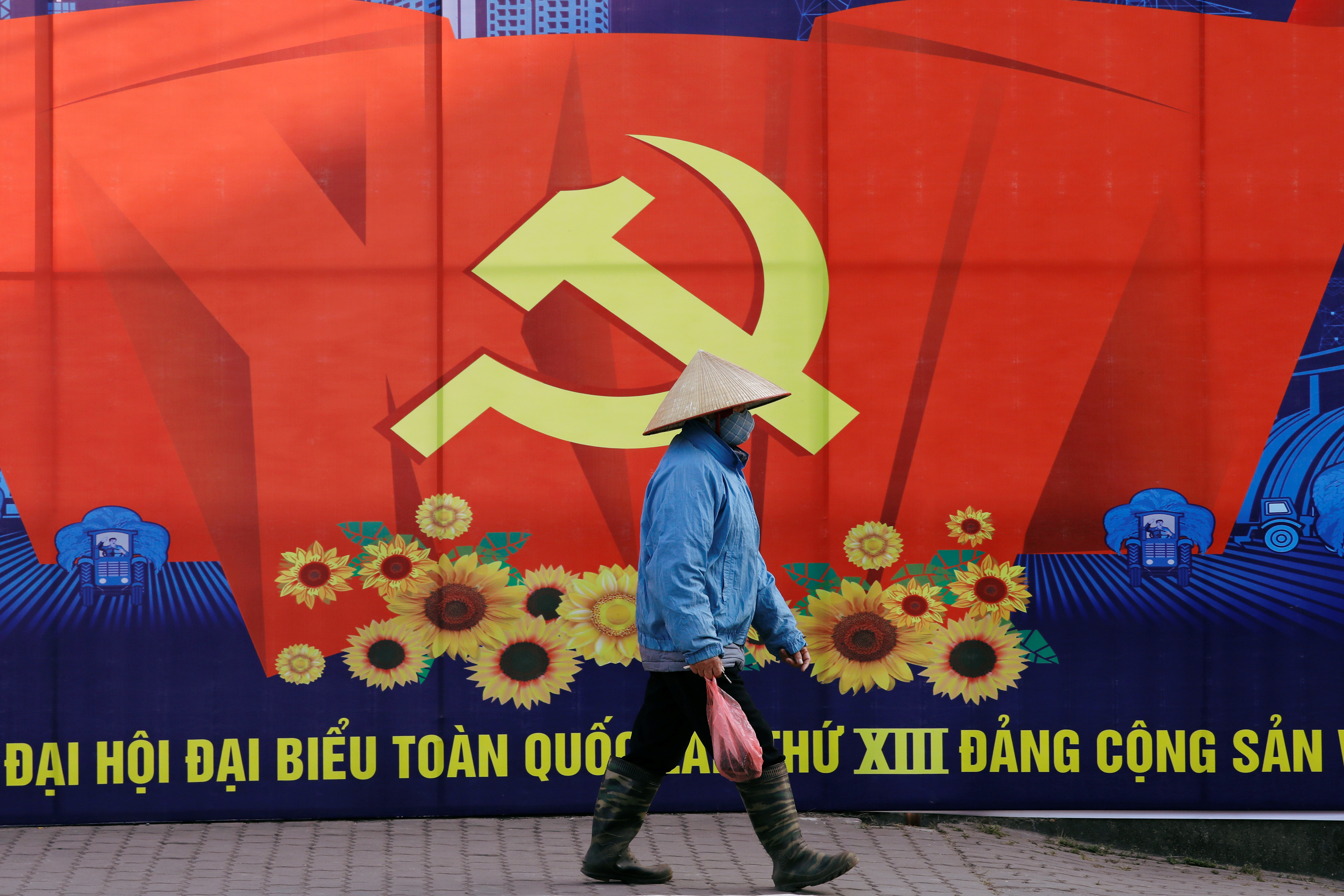 A woman wearing a traditional conical hat walks past a poster for the upcoming 13th national congress of Vietnam Communist Party on a street in Hanoi, Vietnam, January 18, 2021