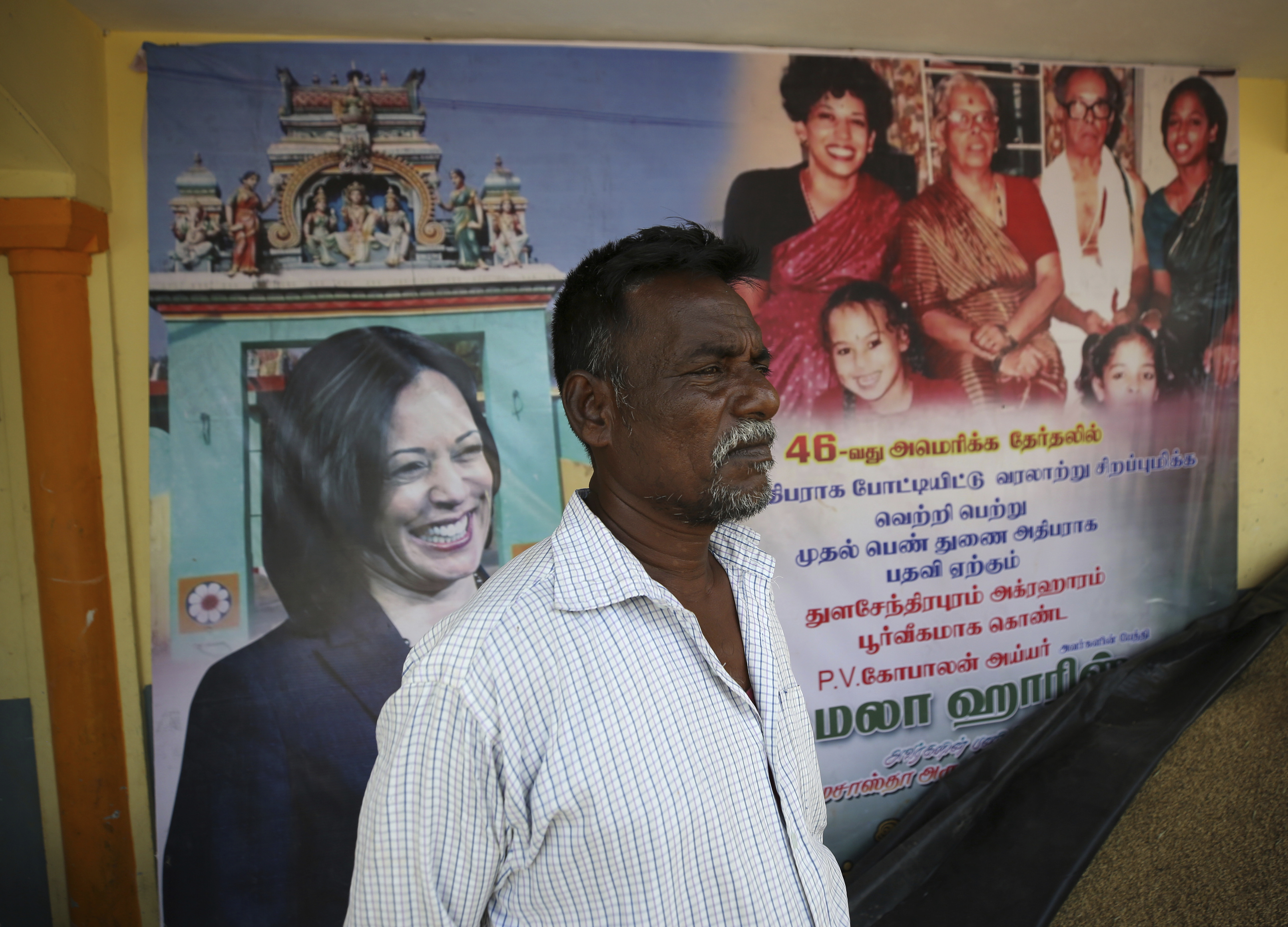 An Indian villager stands in front of a banner displaying photographs of Harris in Thulasendrapuram