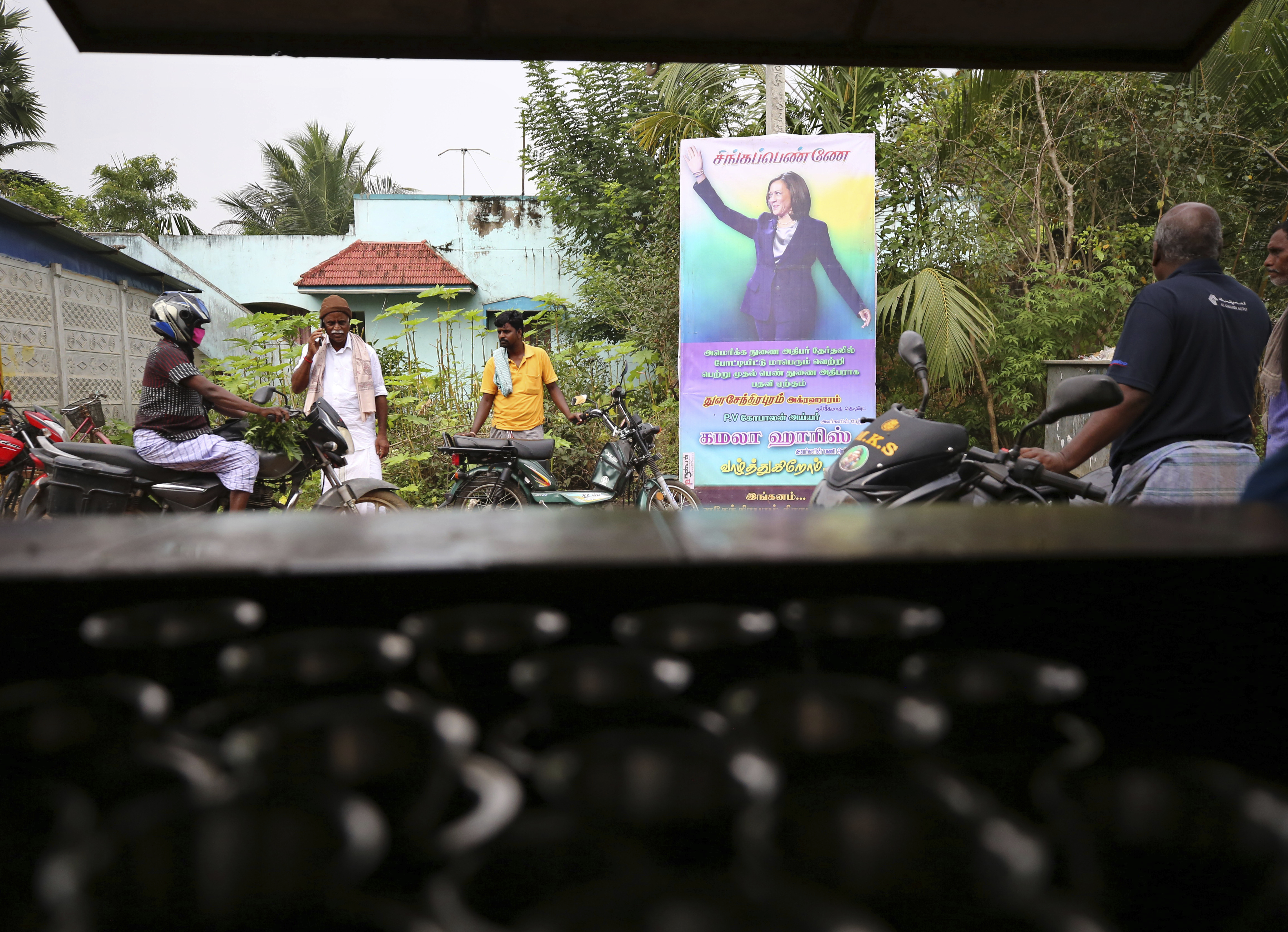 Indian villagers gather outside a local eatery next to a banner featuring Harris in Thulasendrapuram, village