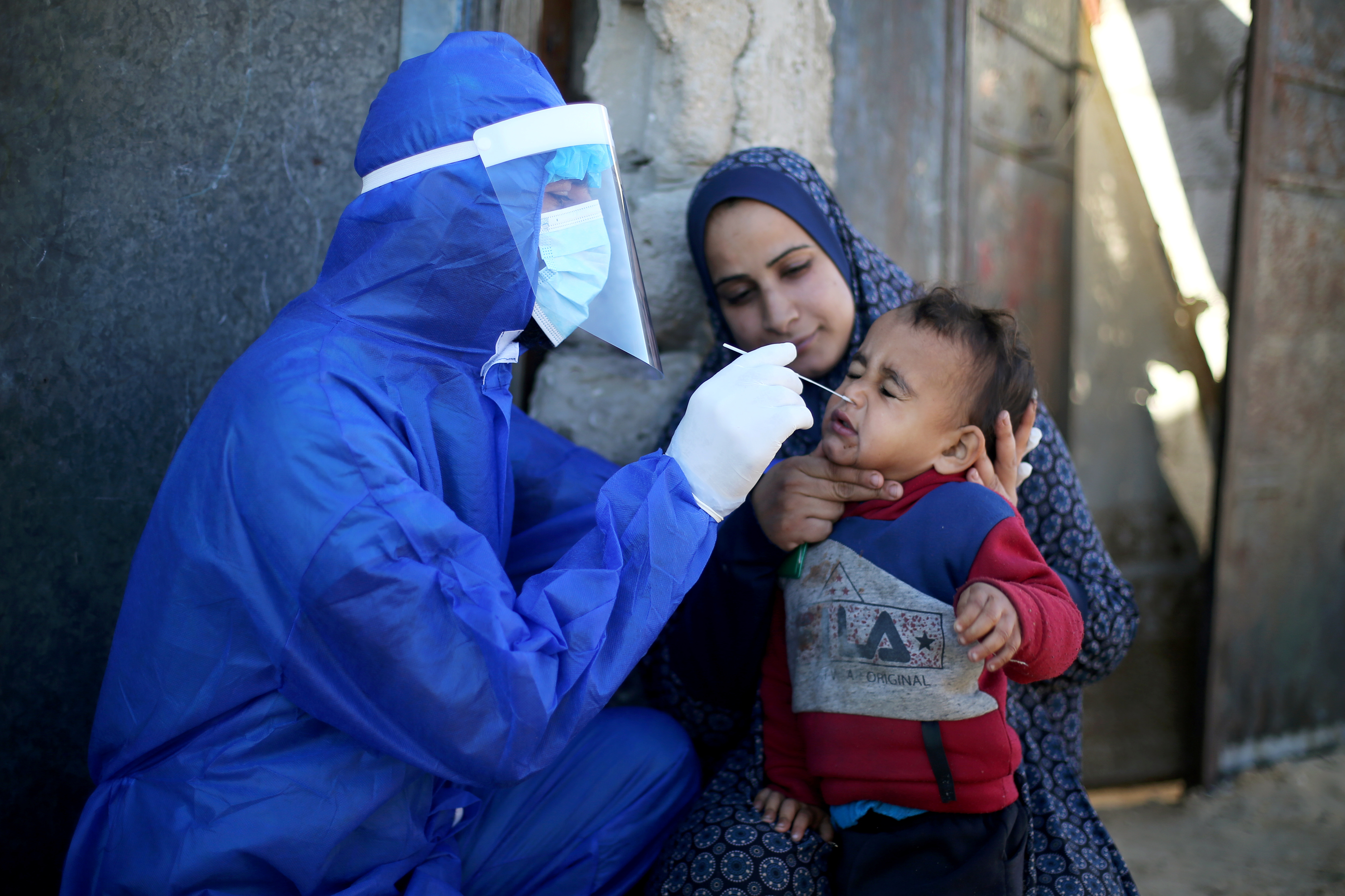 A Palestinian medical worker collects a swab sample from a boy to be tested for the coronavirus disease (COVID-19), in the southern Gaza Strip, January 14, 2021