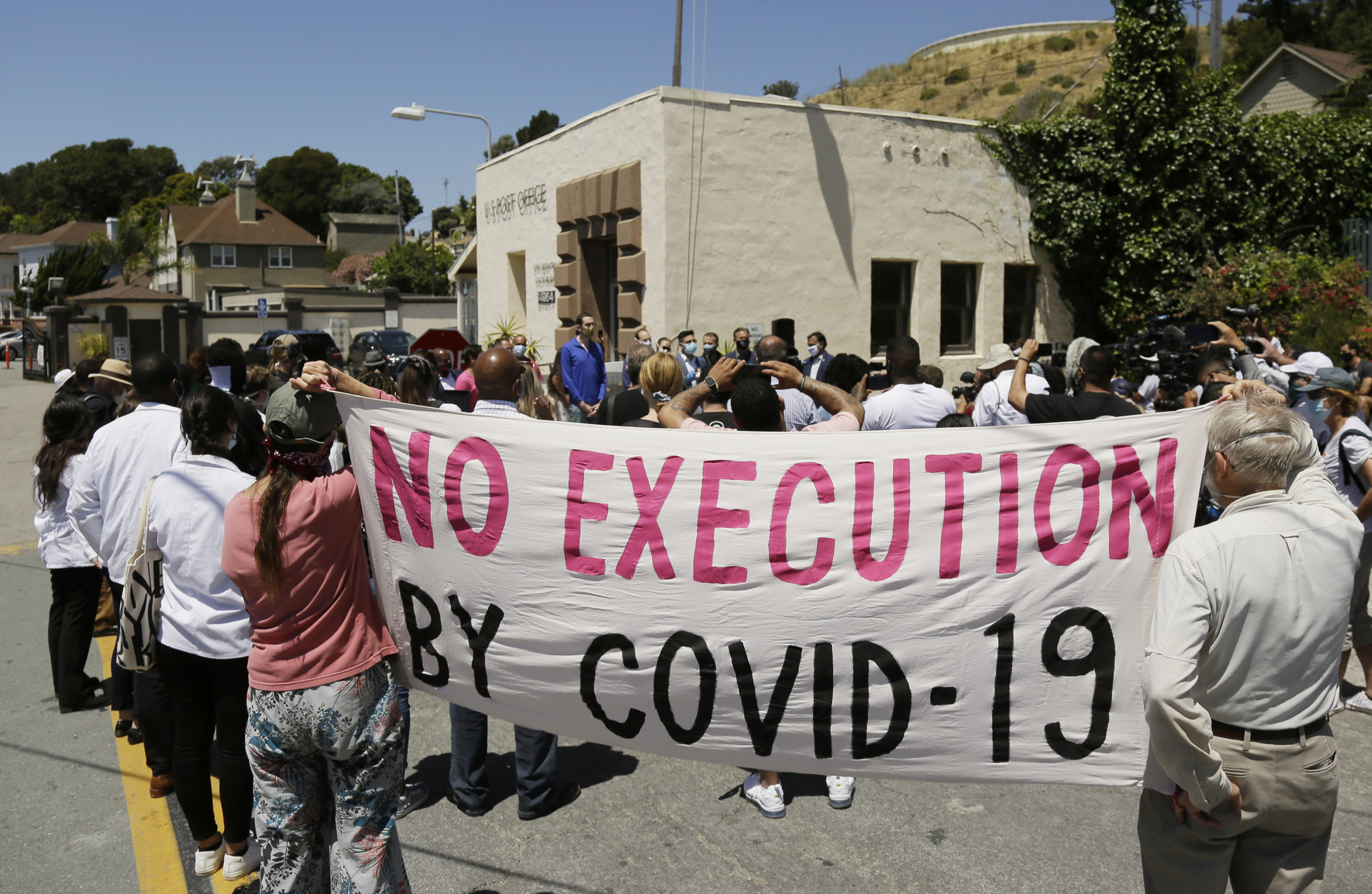 People hold up a banner while listening to a news conference outside San Quentin State Prison in California in July 2020 to discuss a COVID-19 outbreak at the facility that sickened more than 1,400 inmates and caused six deaths