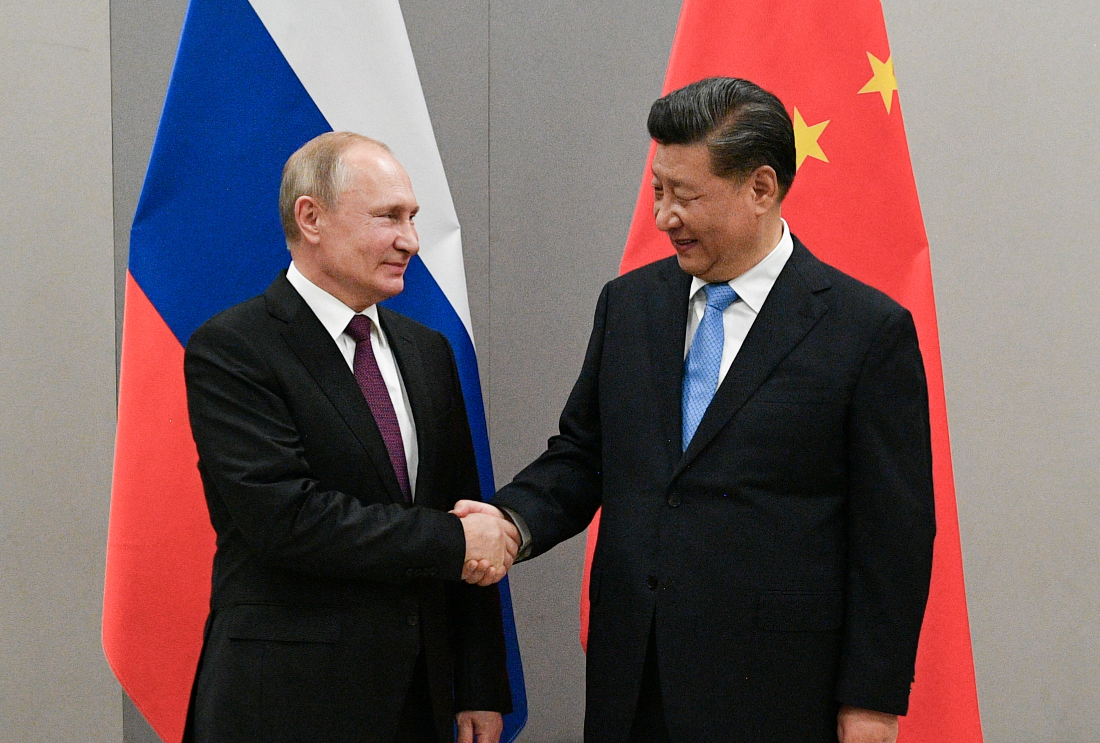 Putin and Xi shaking hands in front of Russian and Chinese flags
