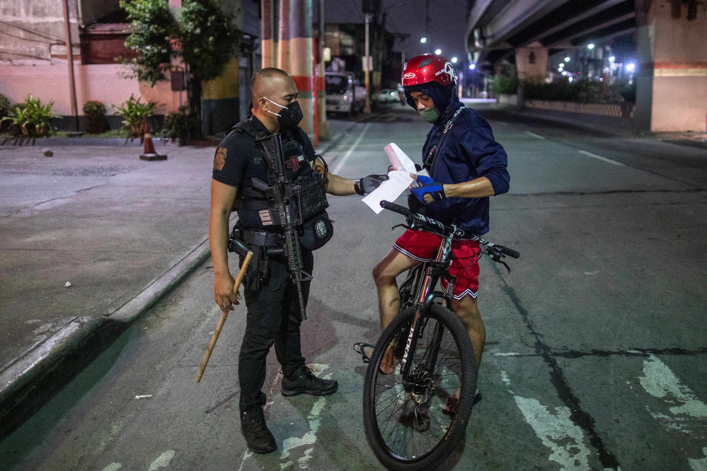 An armed police officer checks the documents of a cyclist at a checkpoint placed to implement a curfew in the country’s capital