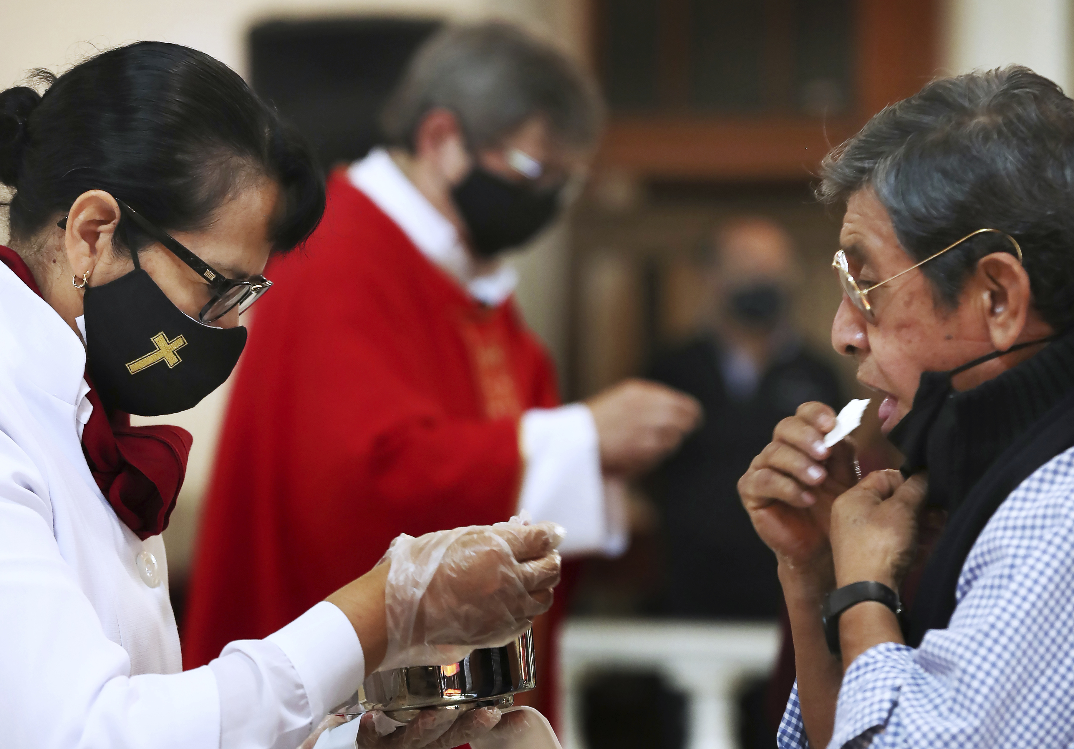 Wearing a mask and wearing plastic gloves to curb the spread of the coronavirus, a woman hands out communion during Palm Sunday Mass at the Iztapalapa Cathedral, a borough on the outskirts of Mexico City