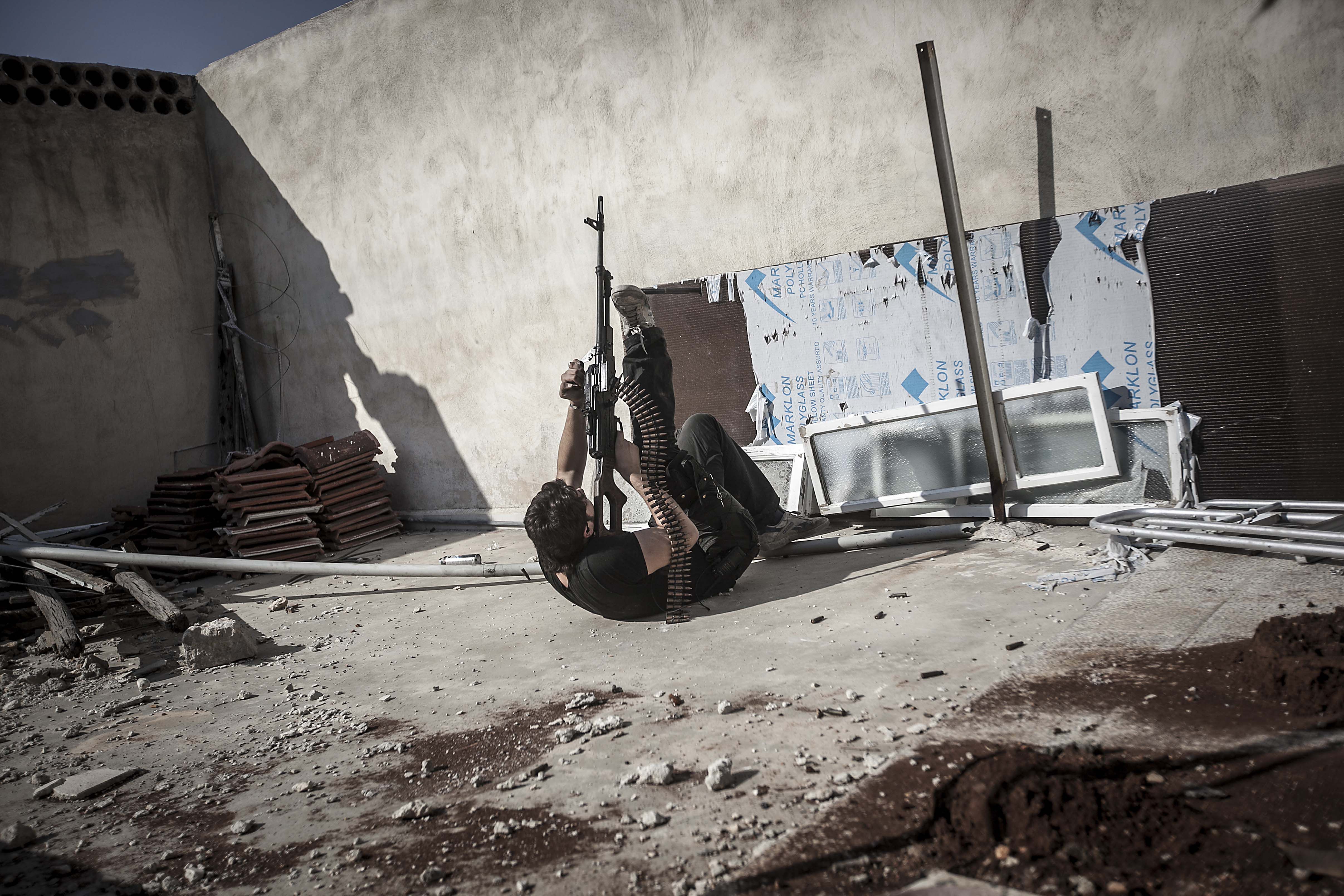 Ali fires a machine gun as an army jet flies in the sky and bombs the rebel positions in the nearby Castel Harami battlefield in the Jdeide district of Aleppo, Syria, in November, 2012 [Narciso Contreras]