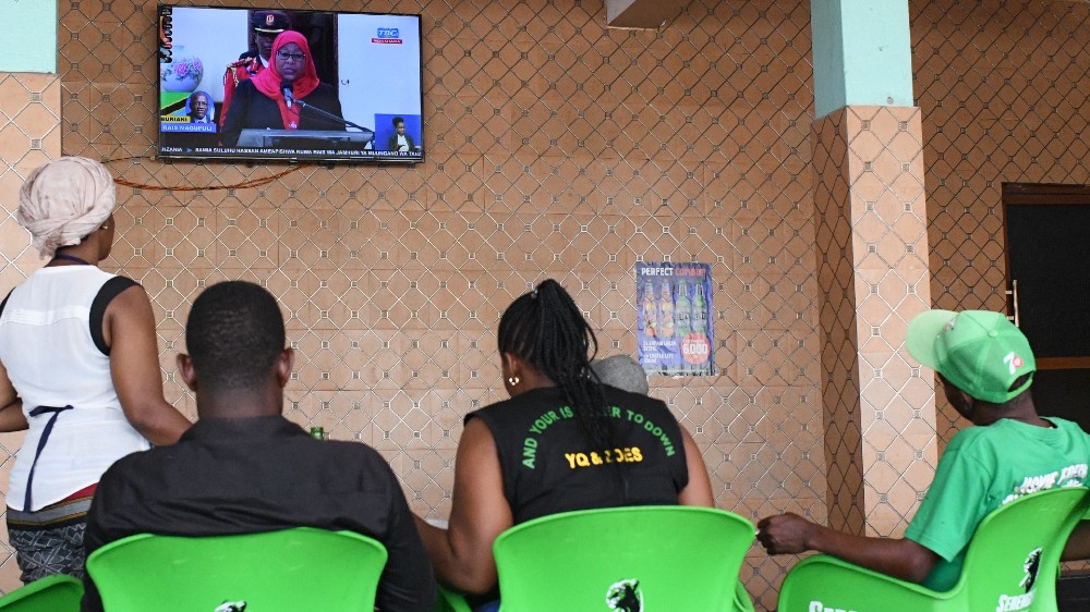 Residents of the Kawe Kanisani district watch the swearing in of new Tanzanian President Hassan [AFP]