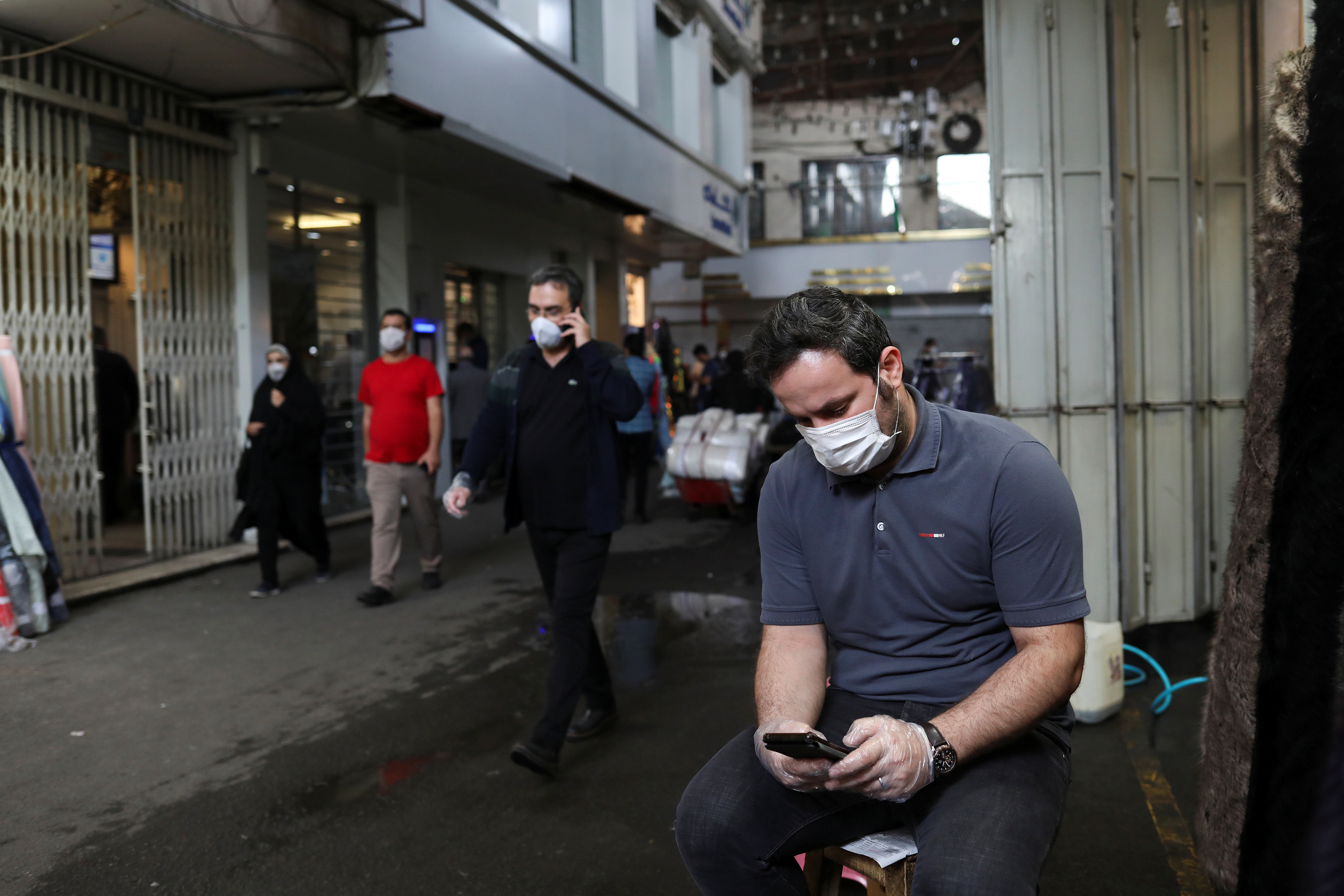 A textile store owner wears a protective face mask, as he uses his phone, following the outbreak of COVID-19 [File: Ali Khara/WANA via Reuters