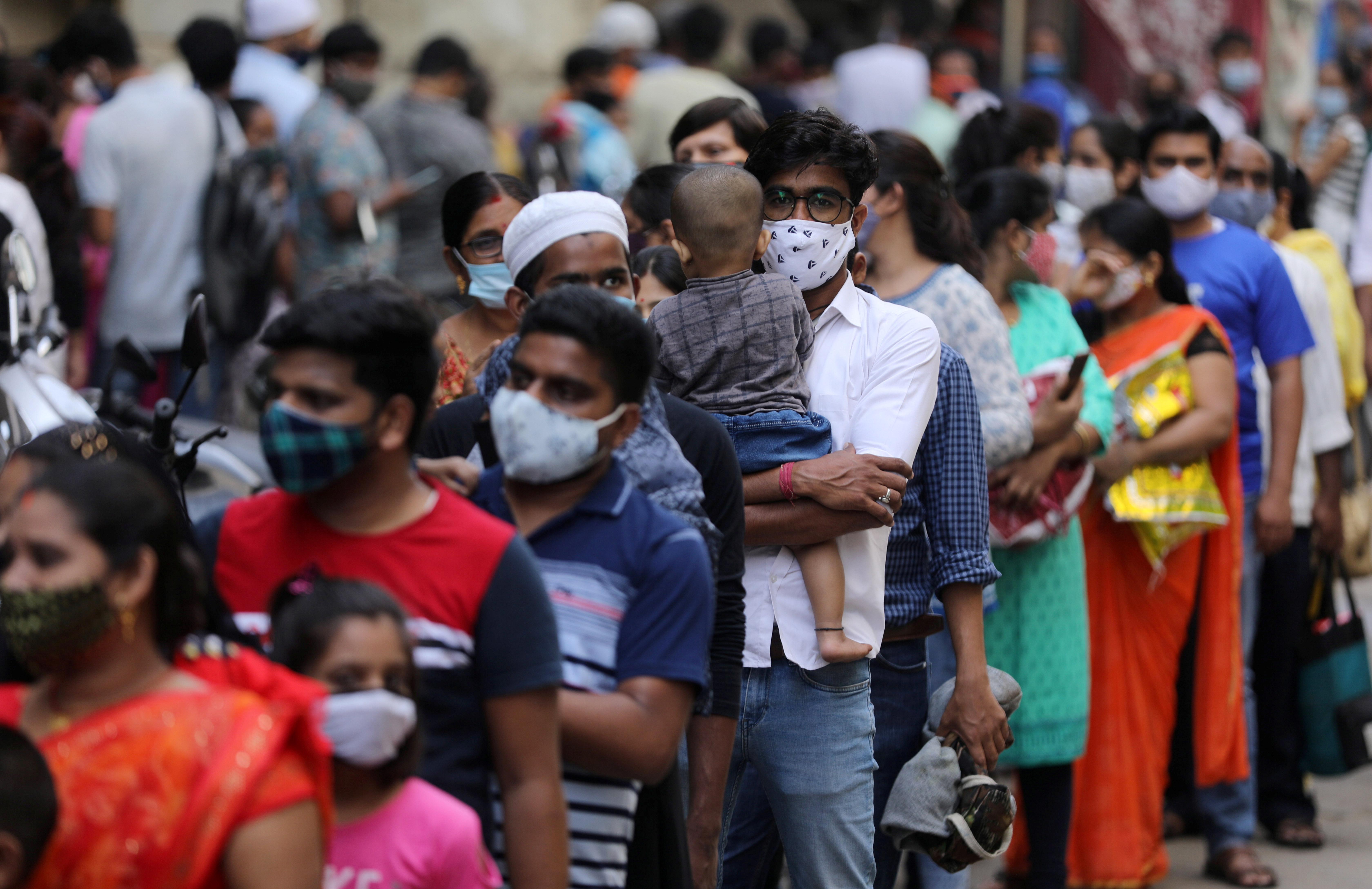People wait in a line to enter a supermarket in Mumbai