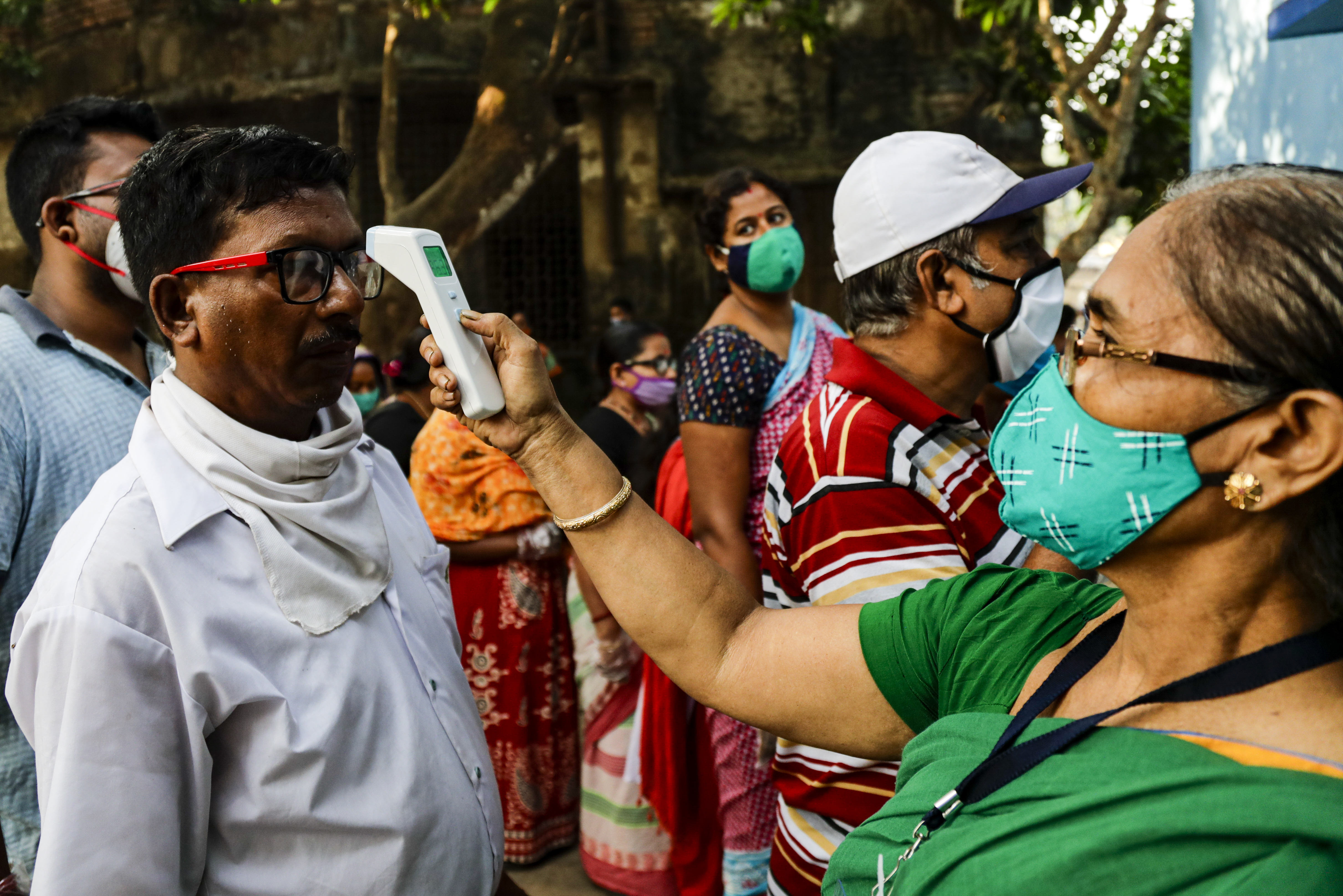 A volunteer takes a voter’s temperature at a polling station in West Bengal’s South 24 Pargana district