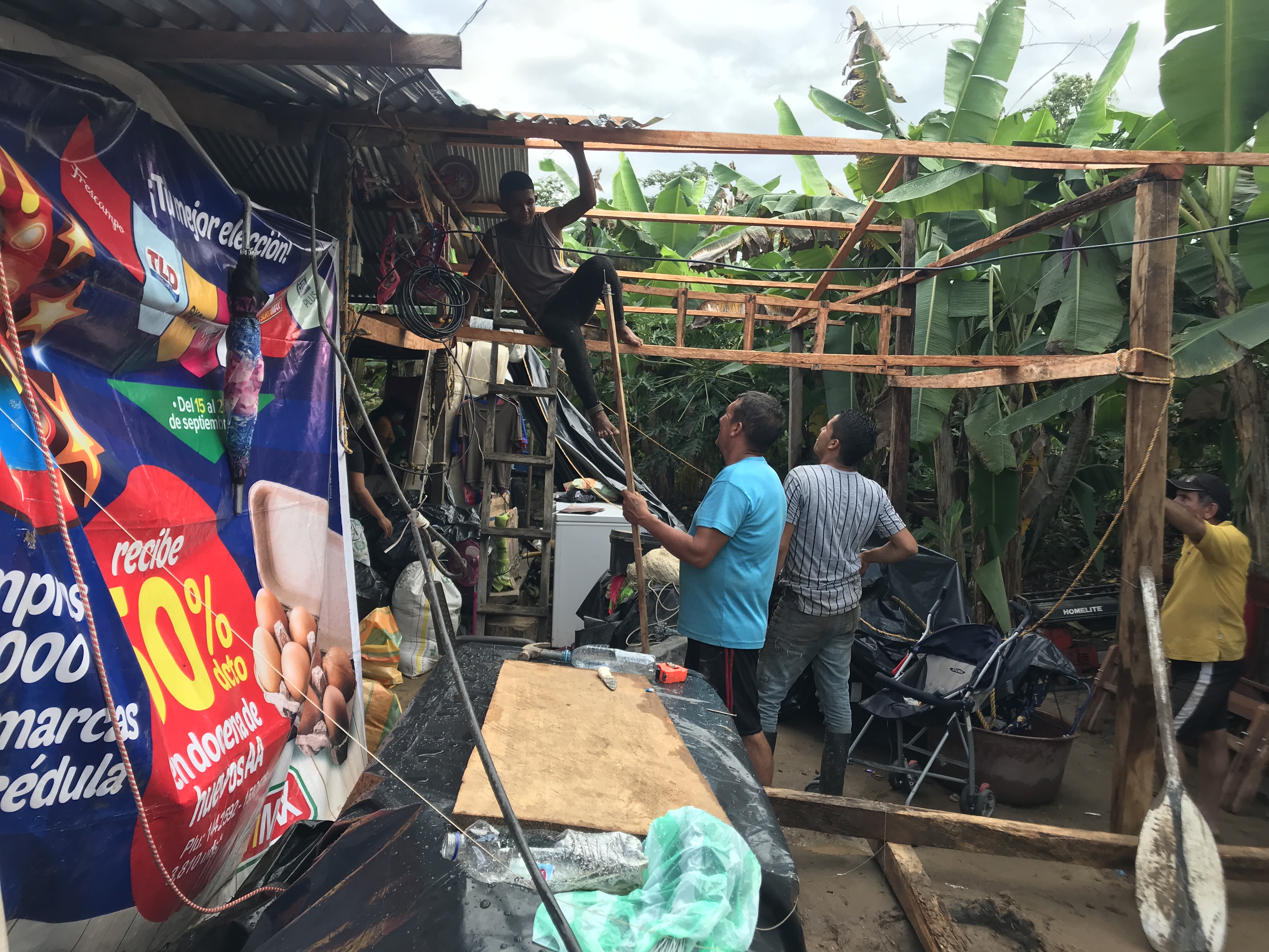 Men build an extension from wood and tin on a makeshift shelter near the riverbank. They decided not to go into the shelters due to fear of COVID and overcrowding