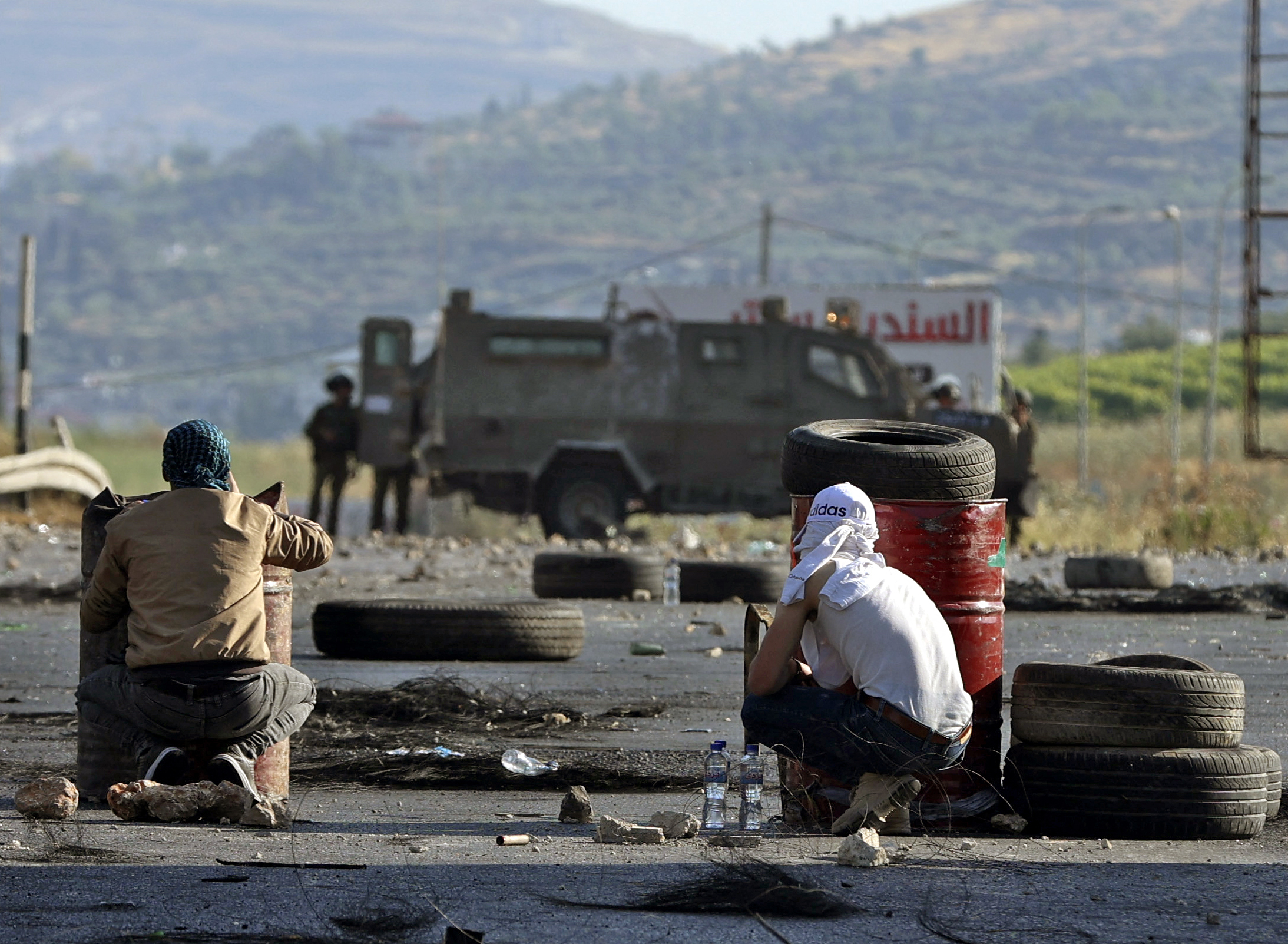 Palestinians take cover during confrontations with Israeli forces near the Hawara checkpoint south of the occupied West Bank city of Nablus