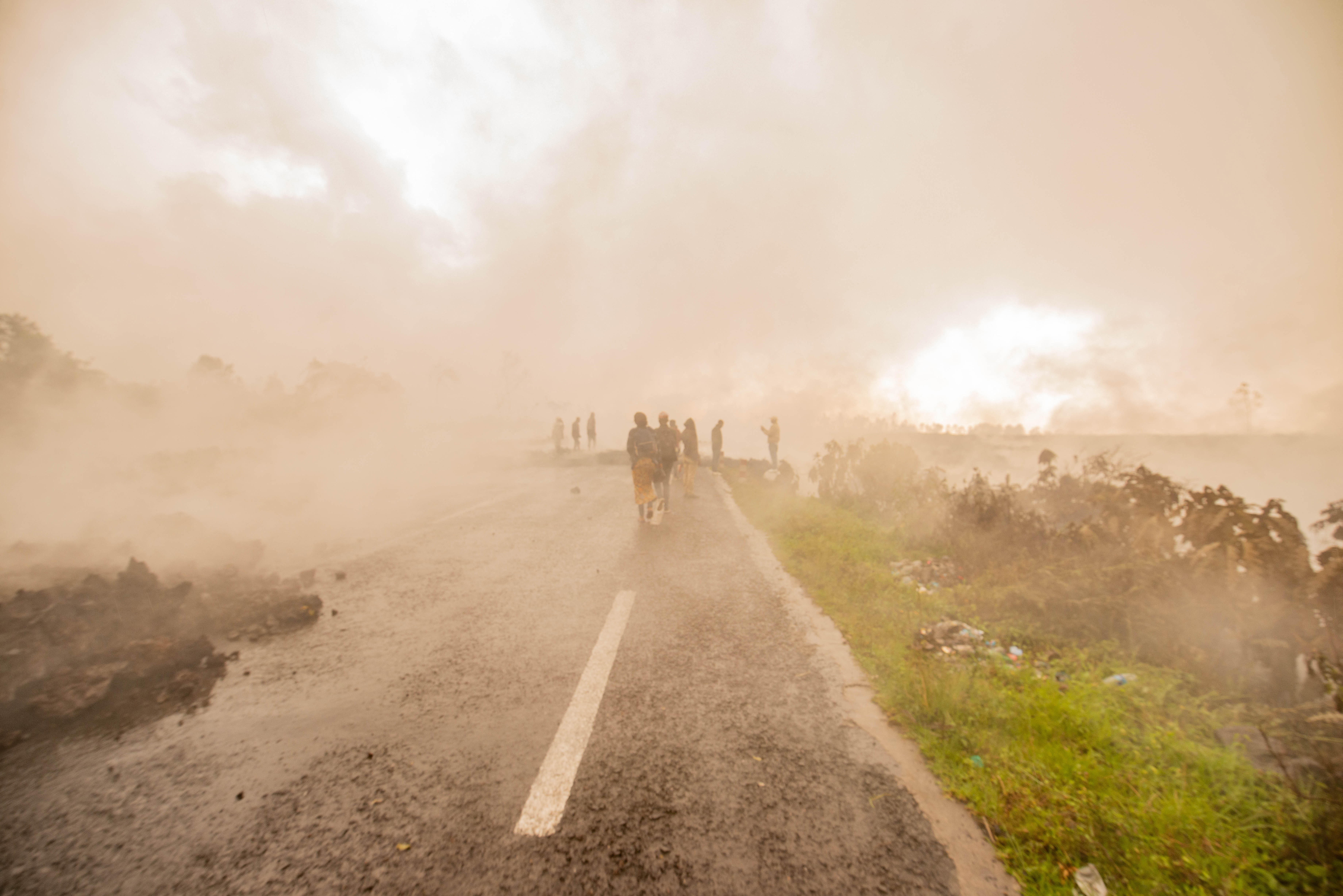 Residents walk through the smoke from smouldering lava flowing from Mount Nyiragongo in Goma [AFP]