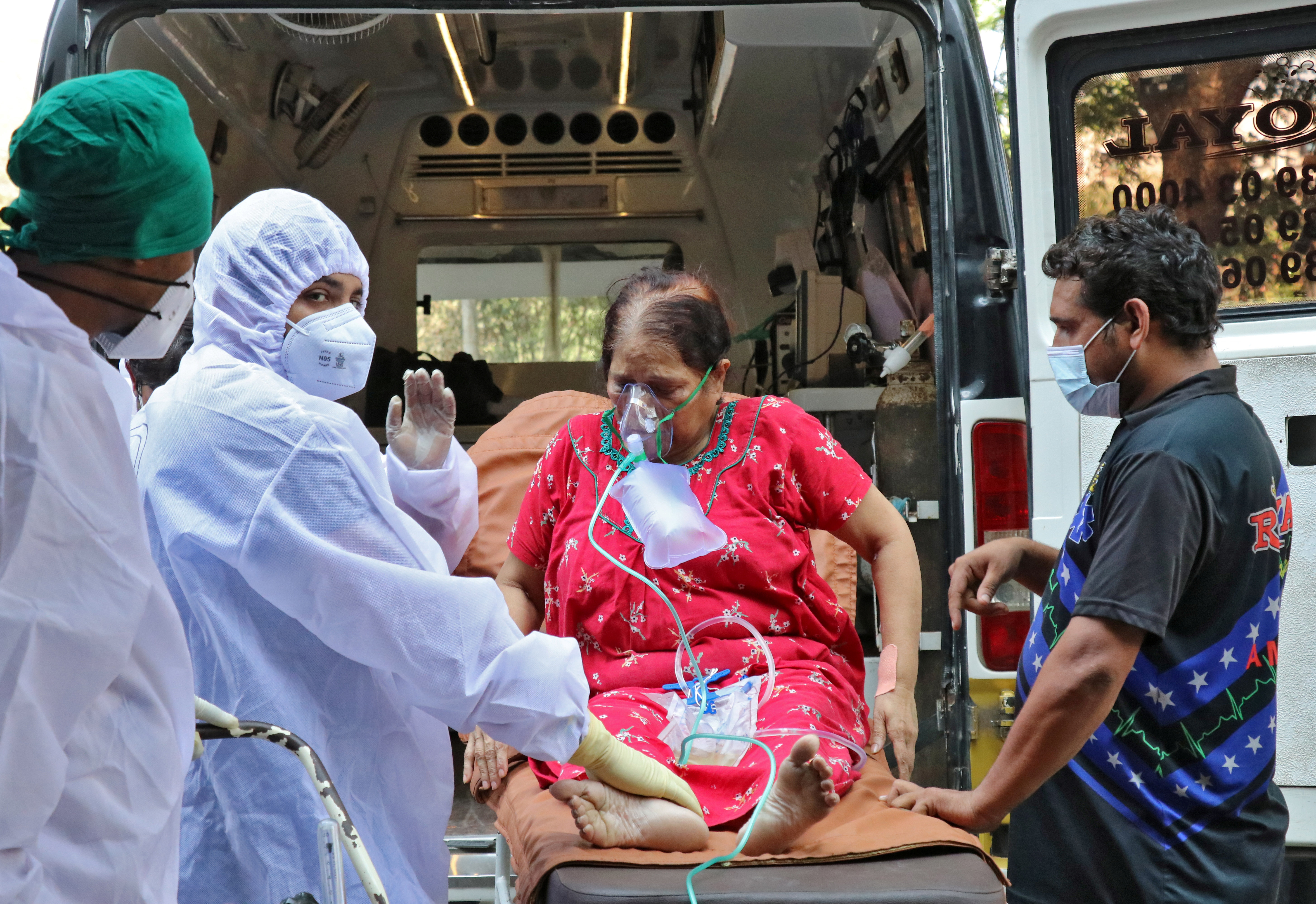 Healthcare workers and relatives carry a woman from an ambulance for treatment at a COVID-19 care facility in Mumbai, India