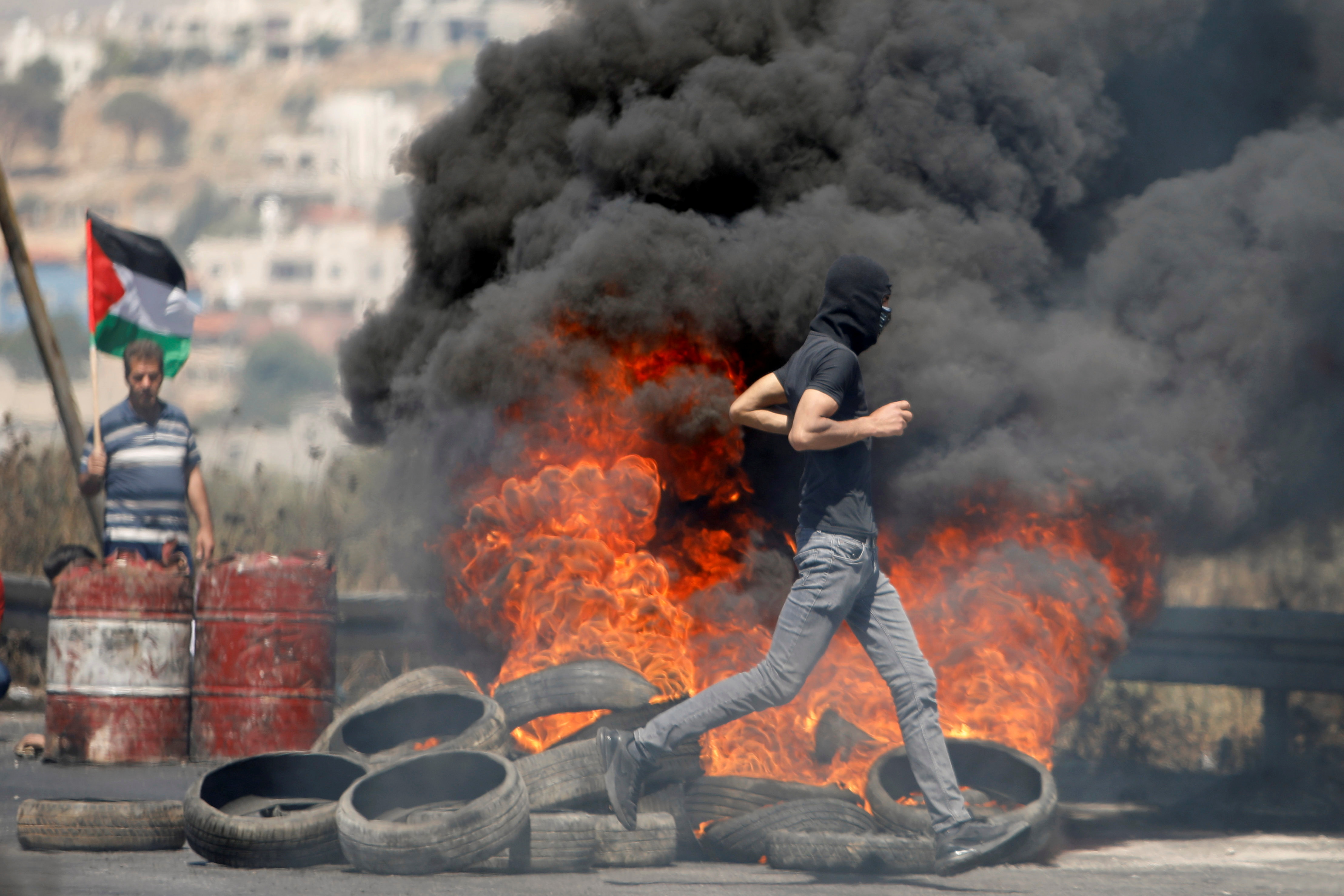 A Palestinian demonstrator runs past burning tyres during a protest over tension in Jerusalem and Israel-Gaza escalation, close to the Hawara checkpoint near Nablus in the Israeli-occupied West Bank