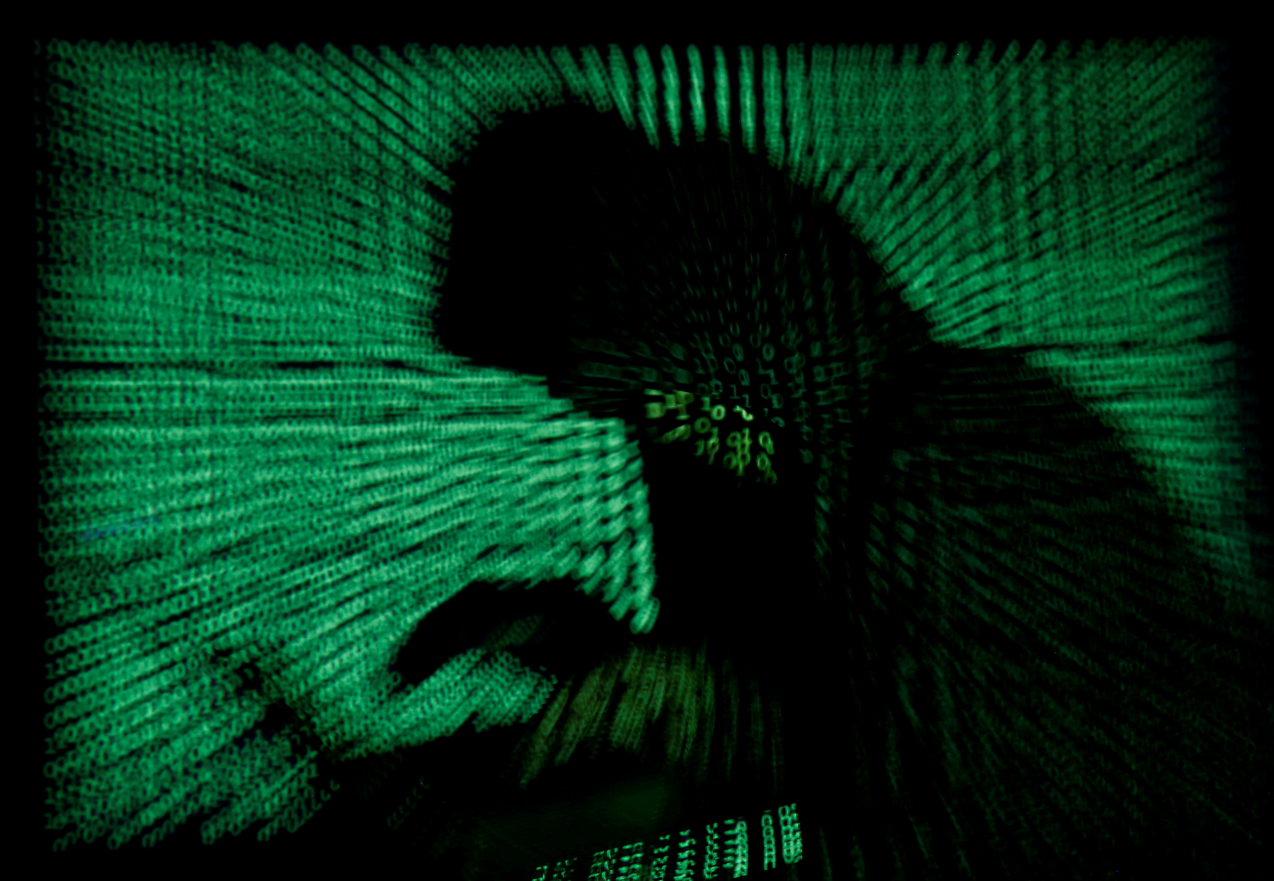 Photo illustration of a hooded man in front of a computer