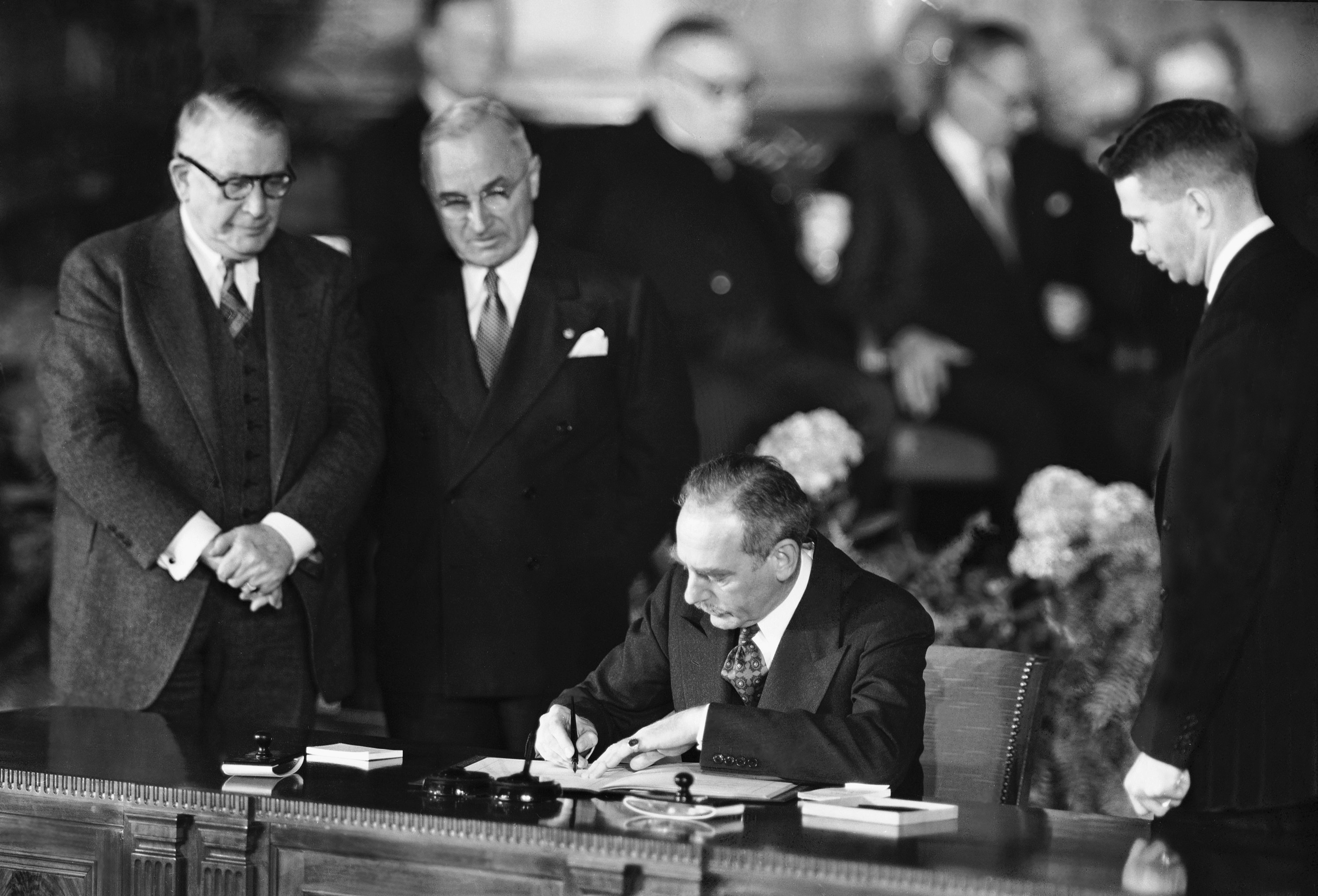 Secretary of State Dean Acheson signs the Atlantic defence treaty for the United States on April 4, 1949, as Vice President Alben W. Barkley, left, and President Harry Truman watch on
