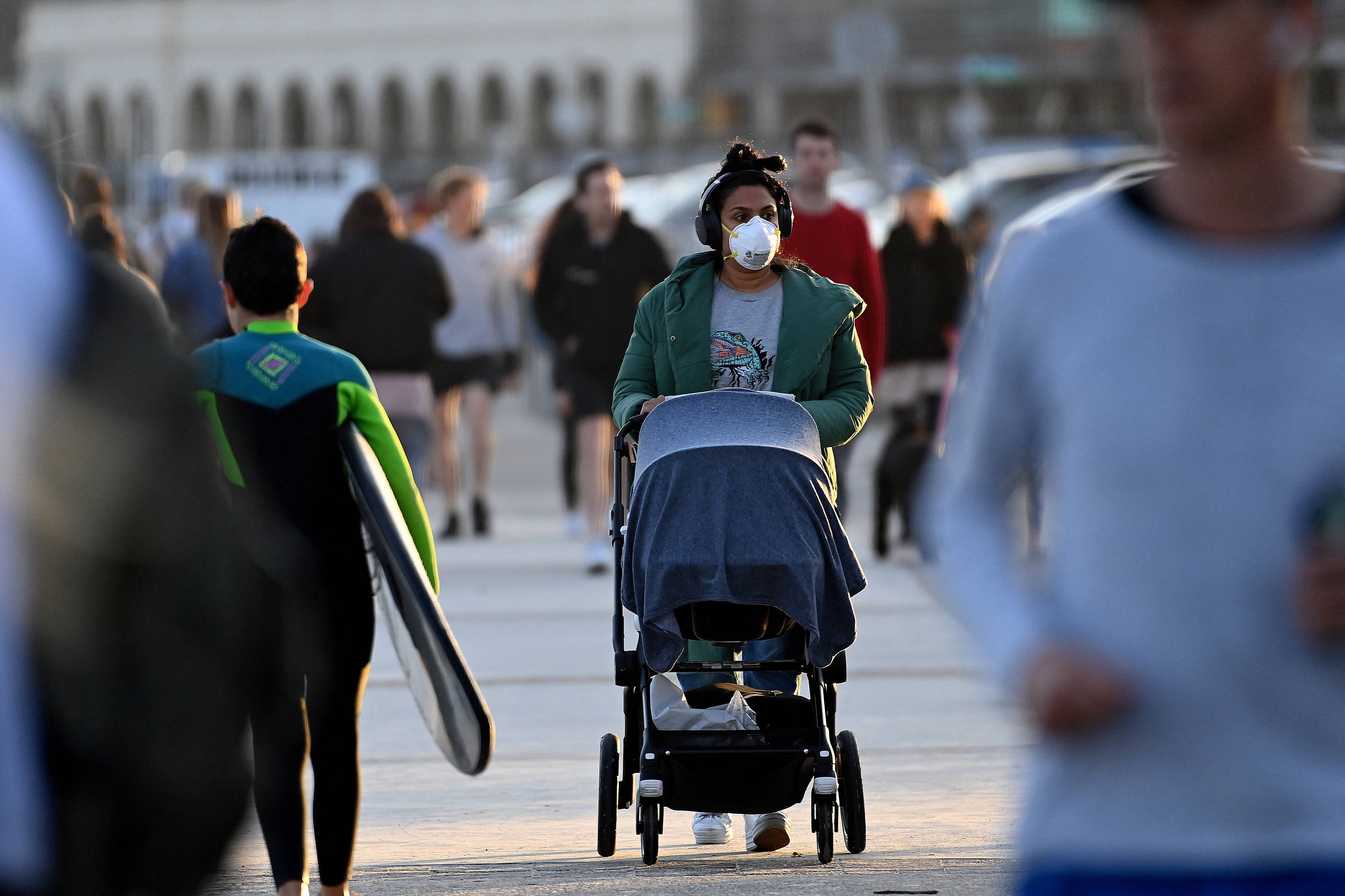 A woman wearing a face mask pushes a pram at Bondi Beach in Sydney