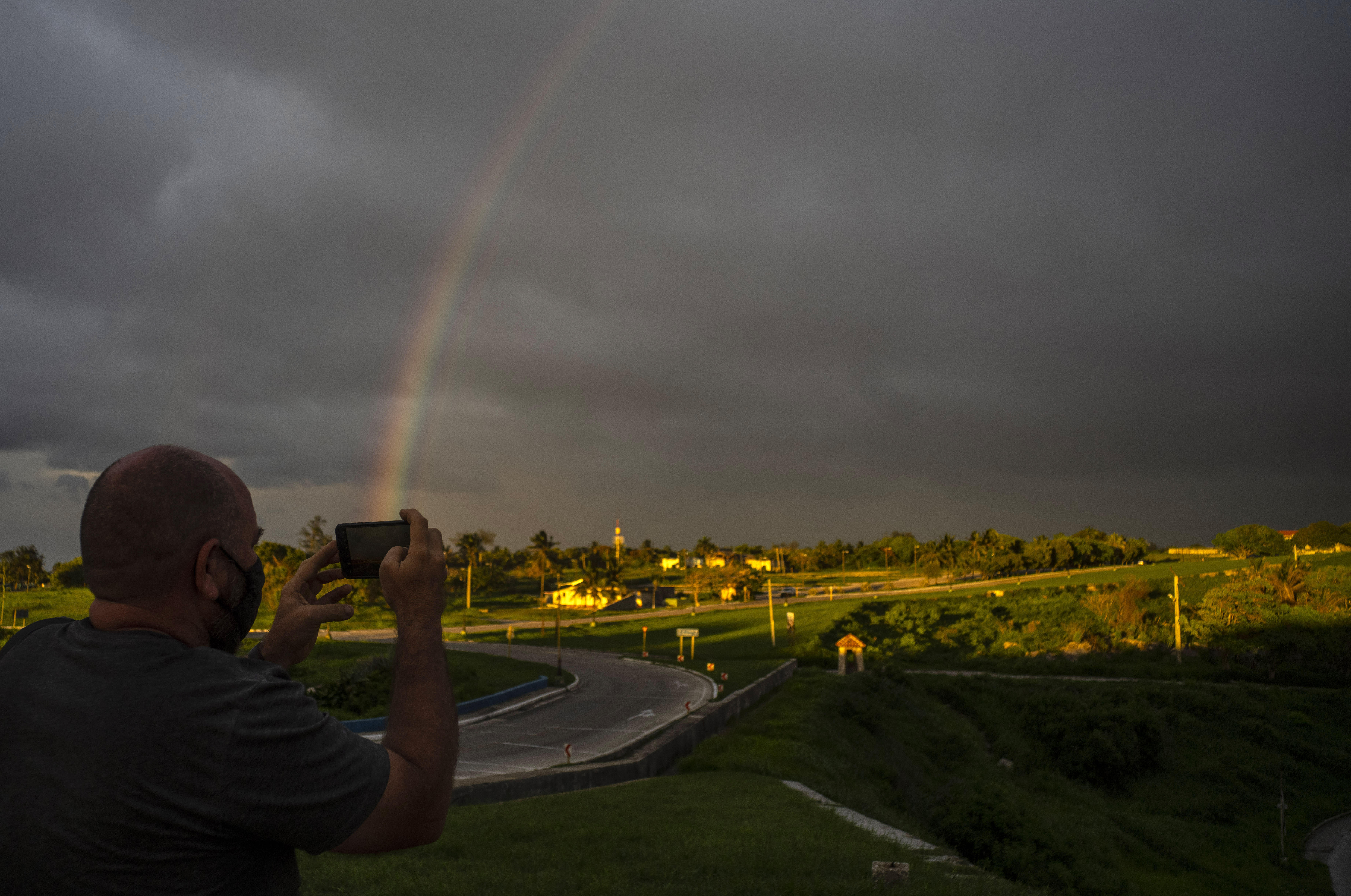 A photographer takes a photo with his mobile phone of a rainbow that came out after the passage of Tropical Storm Elsa, in Havana, Cuba, Monday, July 5, 2021