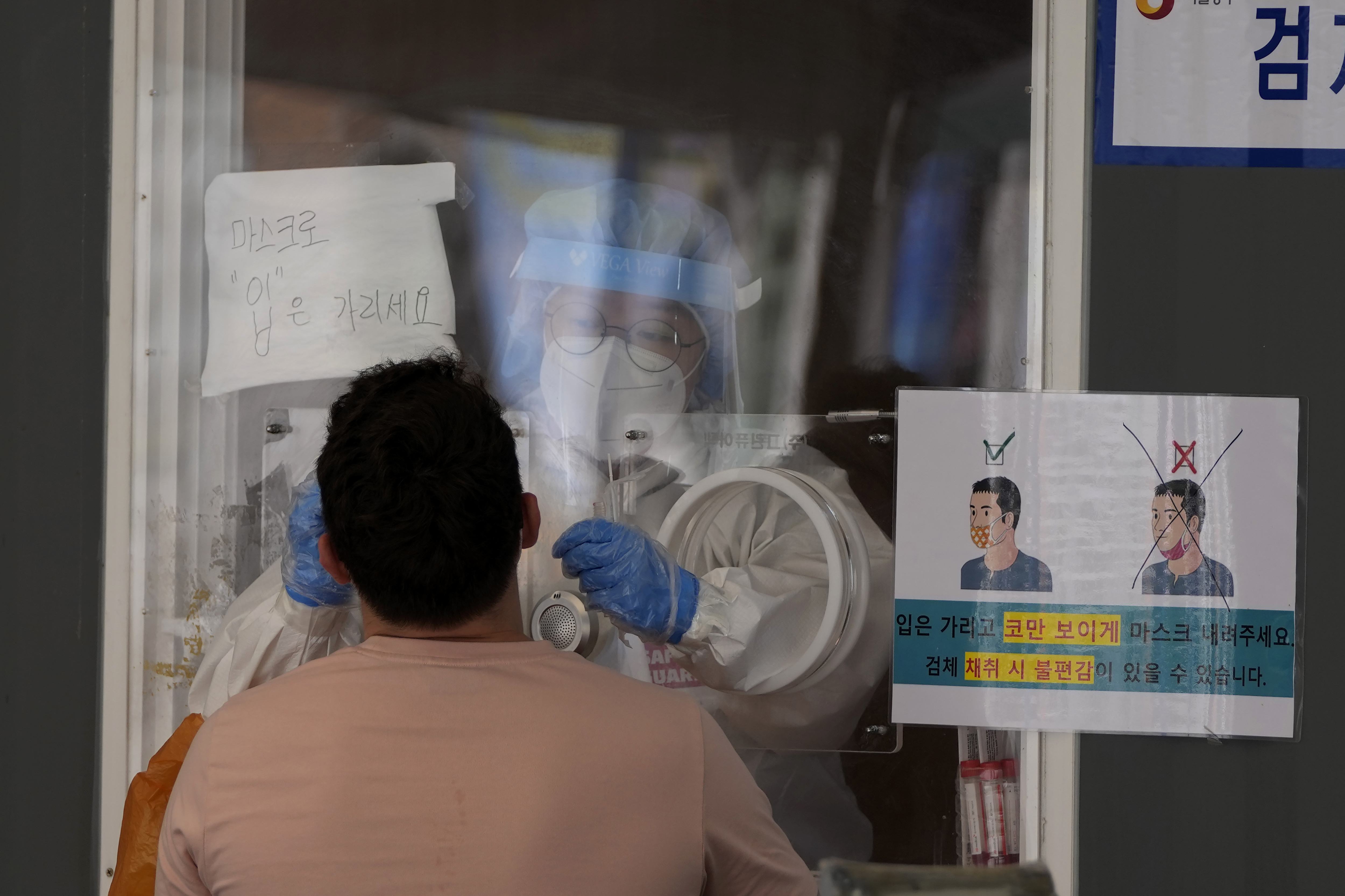 A medical worker wearing protective gear in a booth, takes sample from a man during a COVID-19 testing at a coronavirus testing site in Seoul, South Korea, Wednesday, July 7, 2021