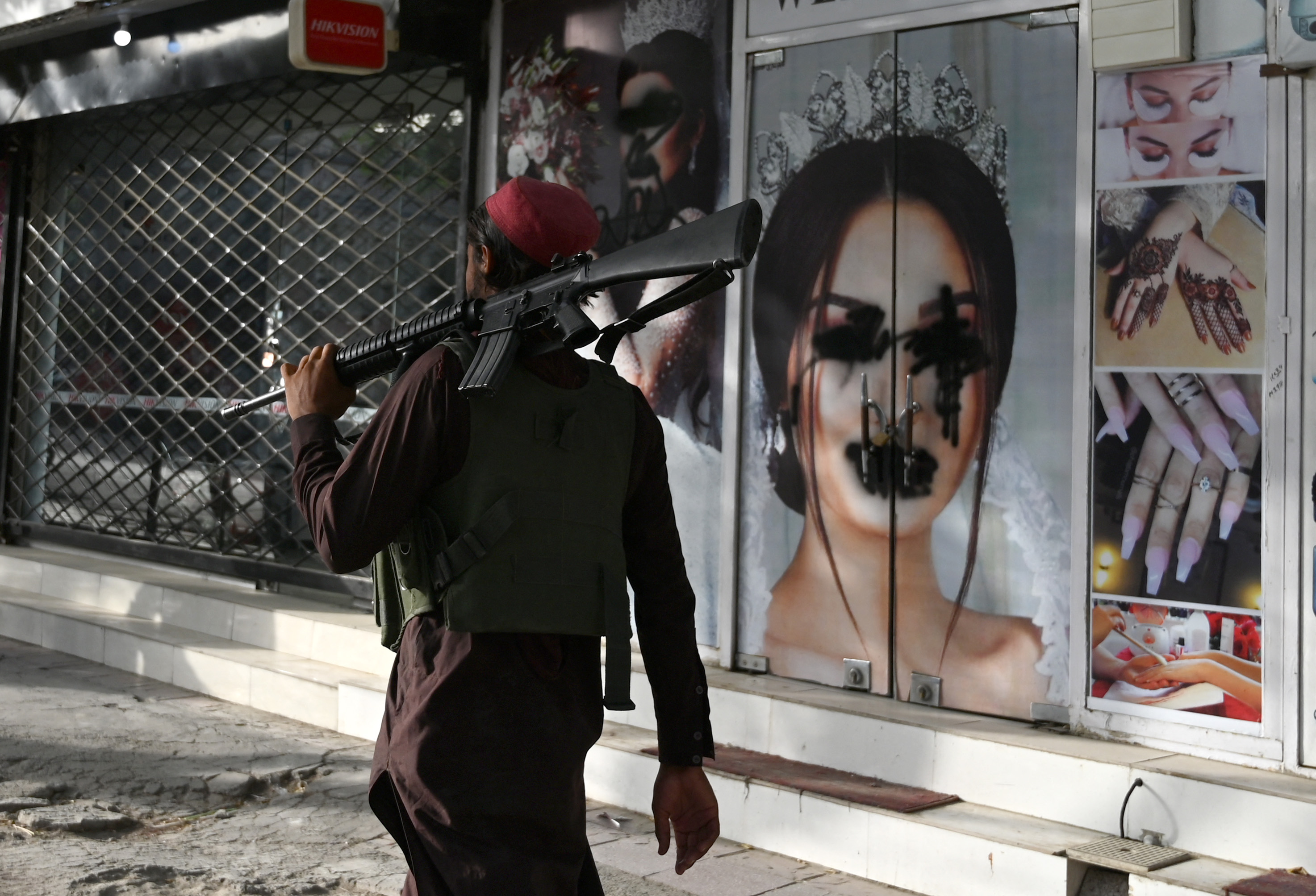 A Taliban fighter walks past a beauty salon with images of women defaced using spray paint in Shar-e-Naw in Kabul