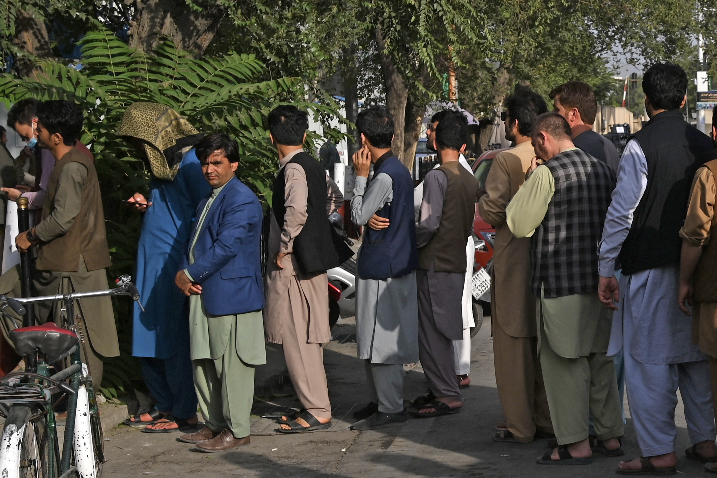 Afghan people stand in a queue as they wait for their turn to collect money from an ATM in front of a bank along a roadside in Kabul [AFP]