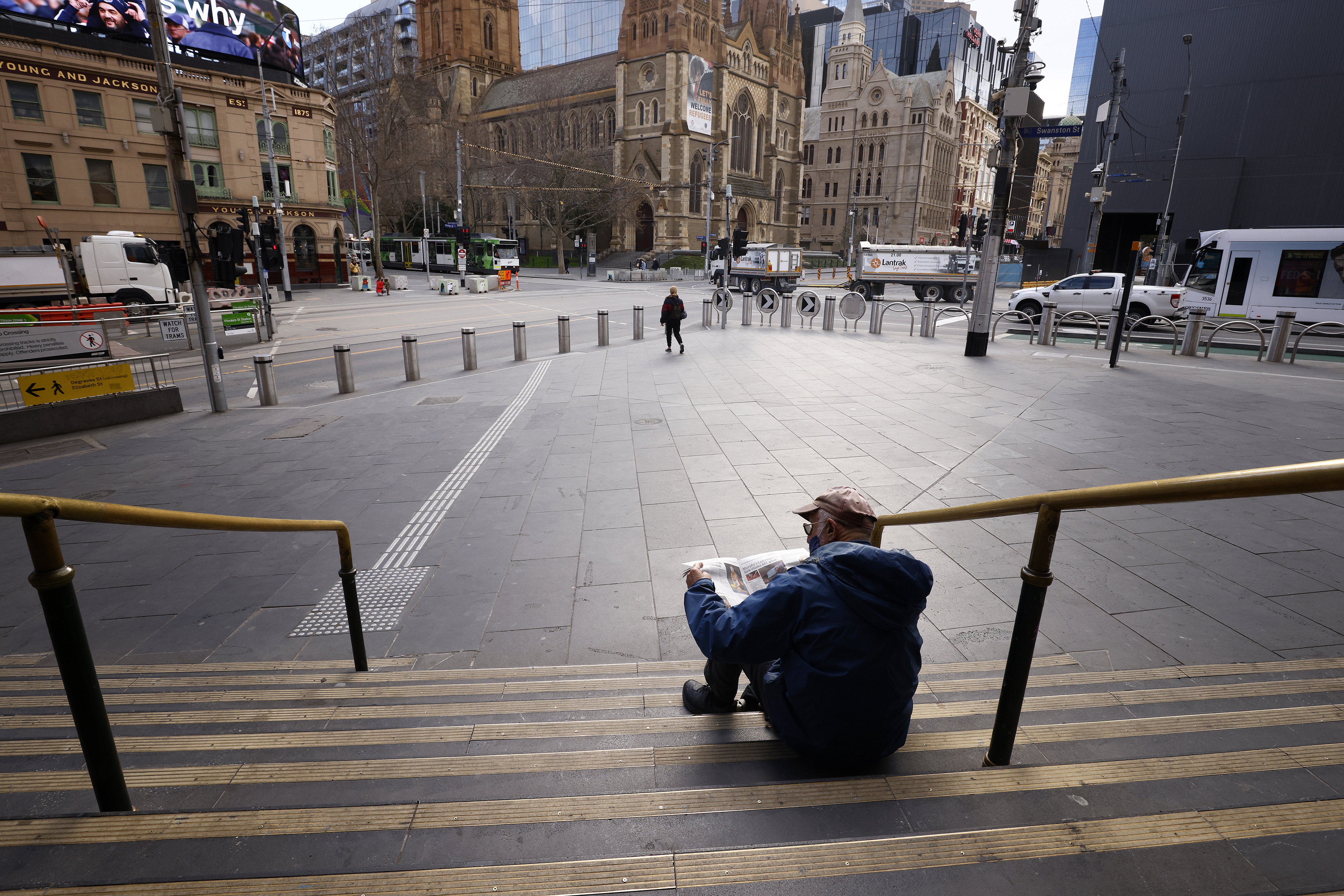 A man reads a newspaper on the steps of Flinders Street Station in Melbourne, Australia, Wednesday, August 11, 2021