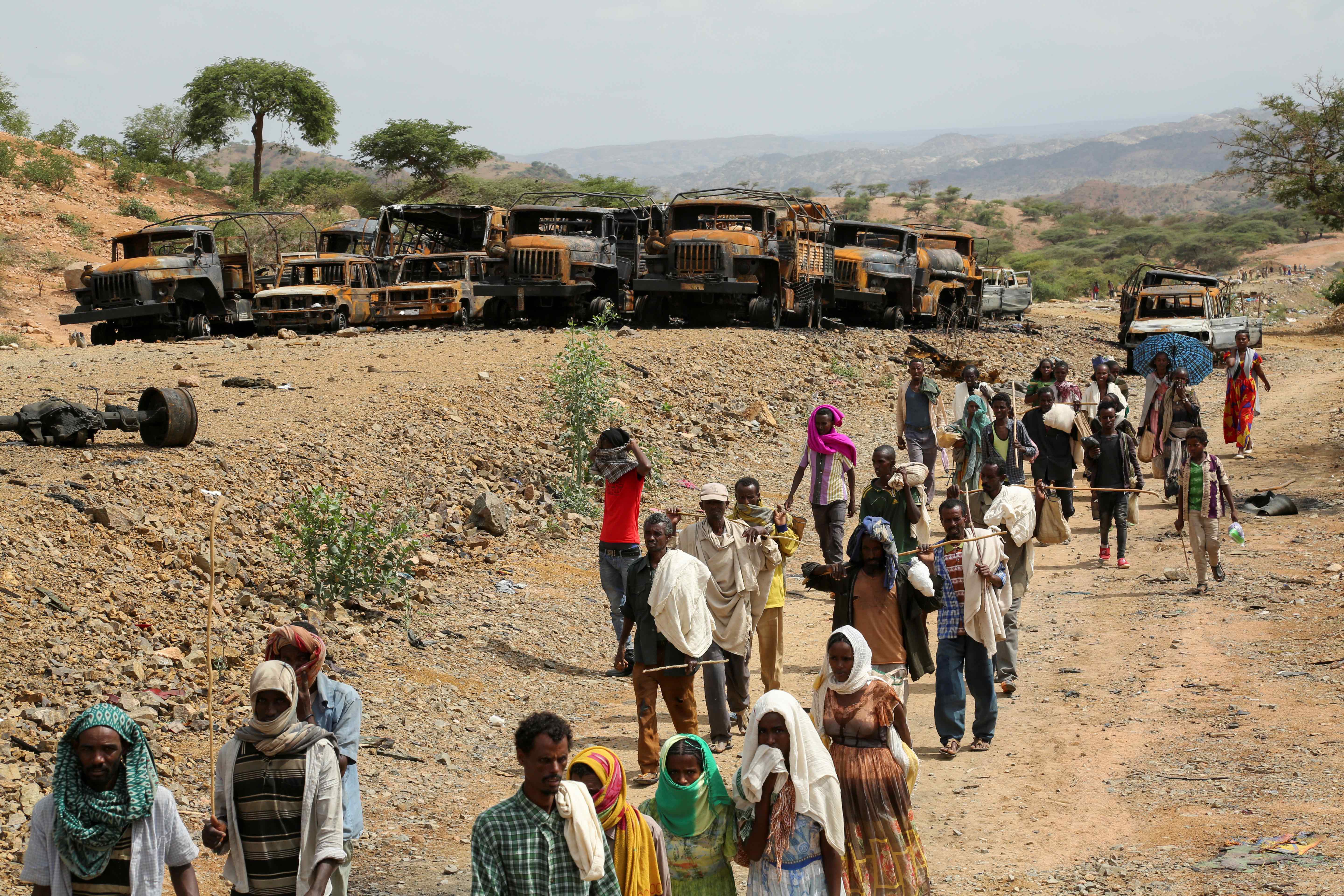 Villagers return from a market to Yechila town in south central Tigray walking past burned vehicles, in Tigray, Ethiopia