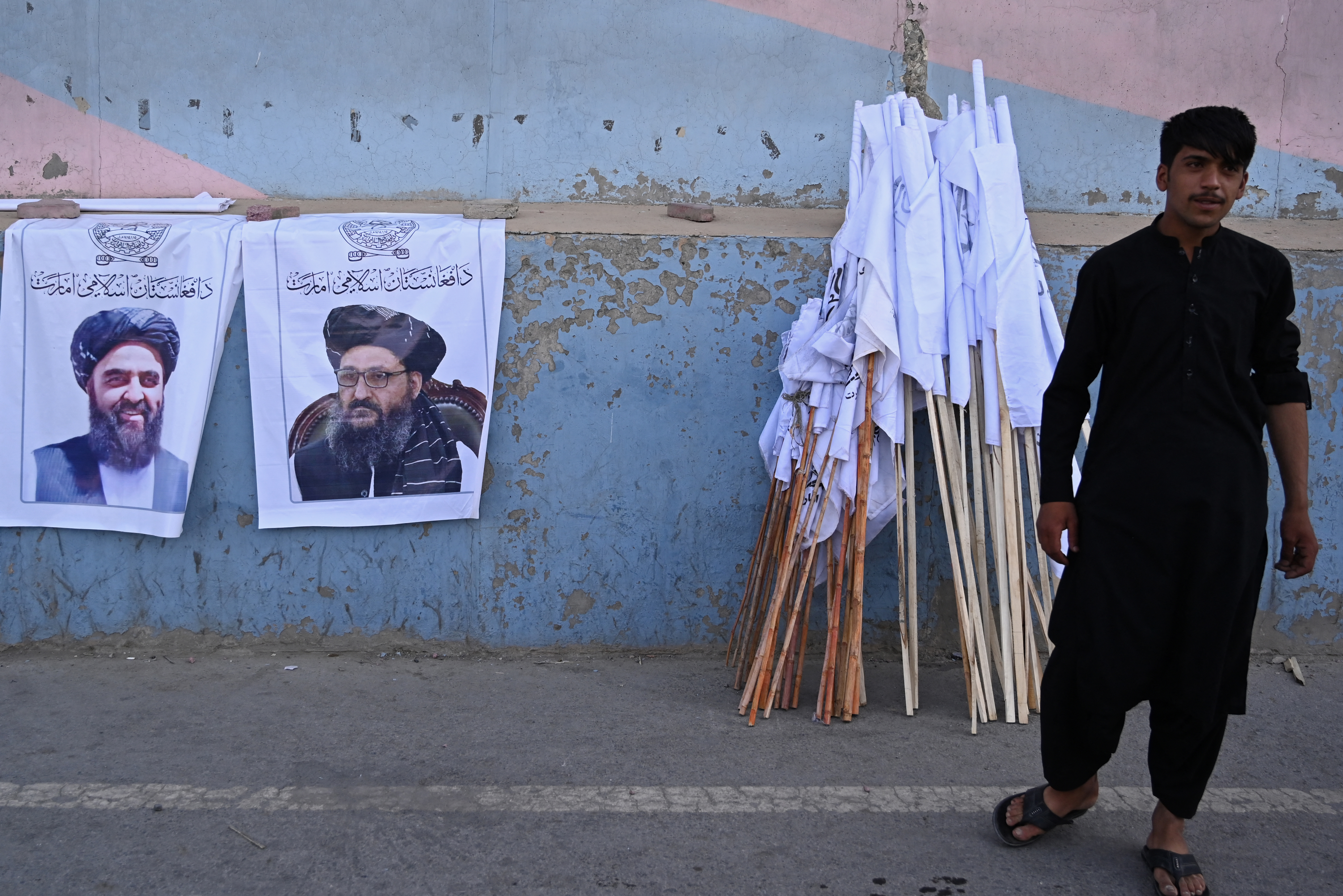 A vendor selling Taliban flags stands next to posters of Taliban leaders Mullah Abdul Ghani Baradar and Amir Khan Muttaqi, left, as he waits for customers along a street in Kabul