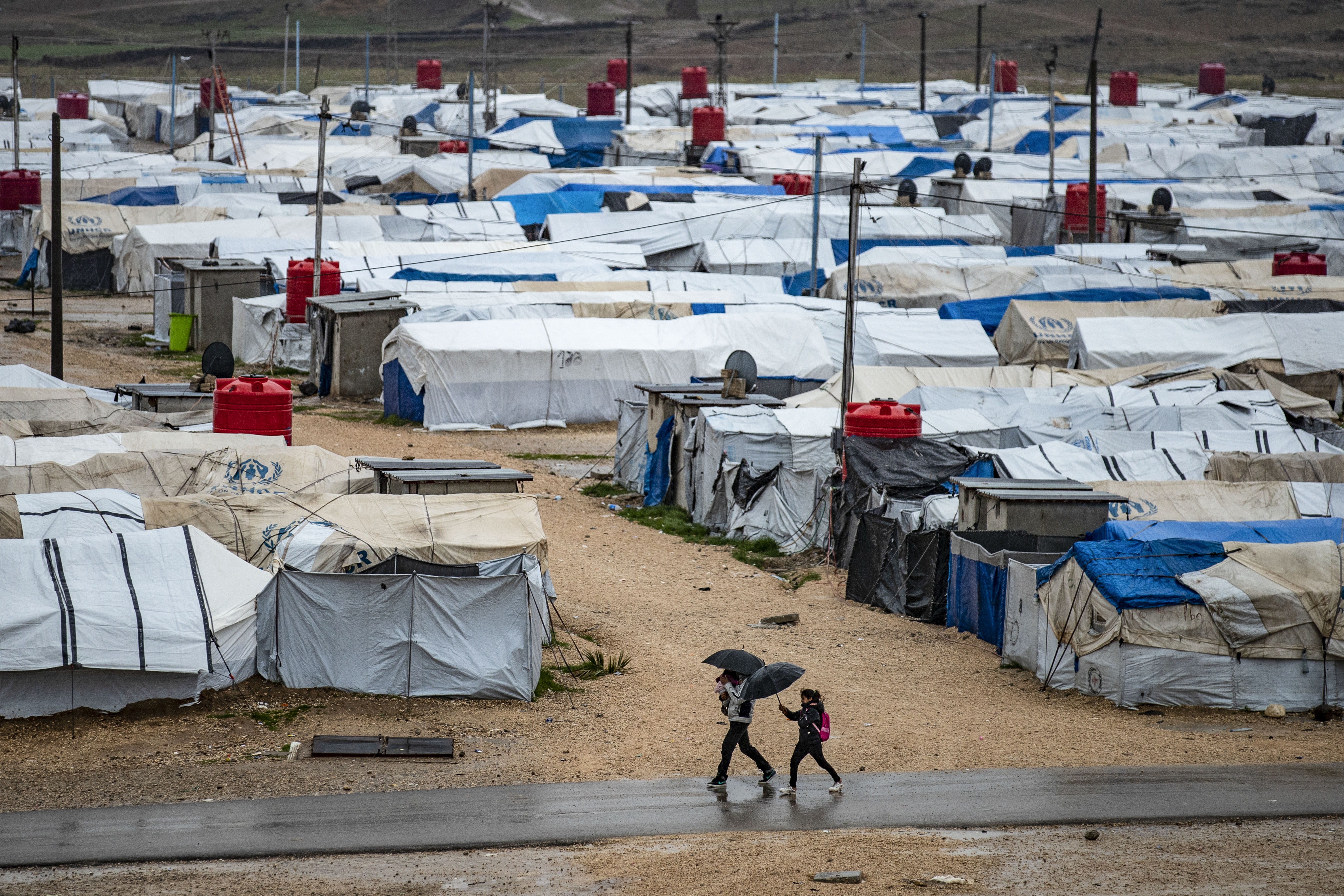 People use umbrellas as they walk in the rain at Camp Roj, where relatives of people suspected of belonging to ISIL (ISIS) are held in Syria's northeastern Hasakah province [File: Delil Souleiman/AFP]